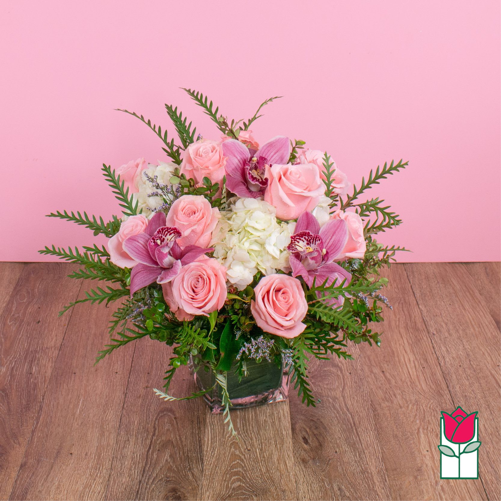 Beretania's Compact Bouquet (Bubblegum) - Elevate your space with the Beretania Florist Compact Bouquet, a charming floral arrangement that effortlessly combines elegance and versatility. Housed in a beautiful 4" glass cube vase, this compact bouquet features a delightful composition of hydrangeas, foliage, and your choice of roses in various colors, allowing you to tailor it to your preferences.  Whether you opt for the timeless allure of red roses, the soft romance of pink, or the vibrant cheerfulness of yellow, each variant of the compact bouquet brings a unique charm to any setting. The meticulous design ensures a harmonious blend of textures and hues, creating a visually appealing arrangement that suits any occasion.  For those seeking an extra touch of sophistication, consider our upgraded option – the Olivia Compact Bouquet. This variant remains true to the original design but introduces the exotic beauty of colorful cymbidium orchid blossoms, elevating the bouquet to a new level of elegance.  Perfect as a thoughtful gift or a stunning addition to your own space, the Beretania Florist Compact and Olivia Bouquets are crafted with precision and care, promising a burst of floral beauty that suits your style and preferences. Choose the color that speaks to you and let the timeless beauty of these bouquets brighten your day.