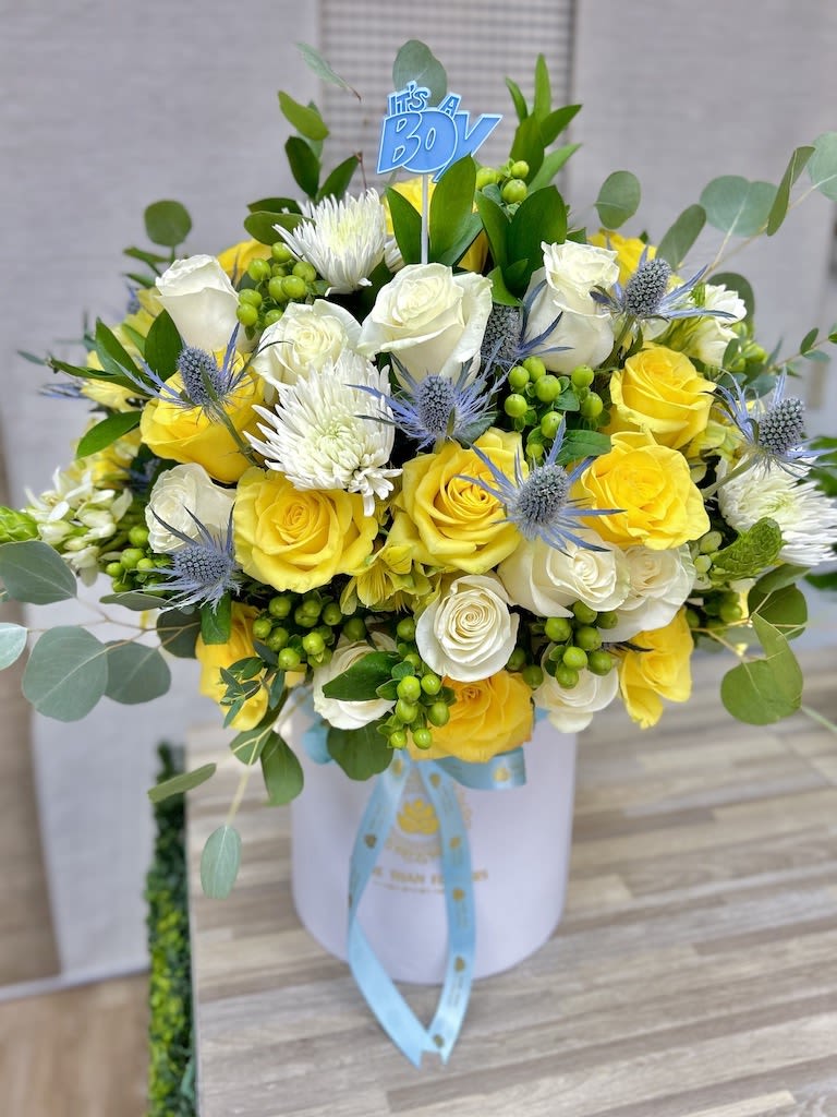 Hatbox arrangement of yellow and white roses with mums, blue thistles, and an It’s a Boy pick.