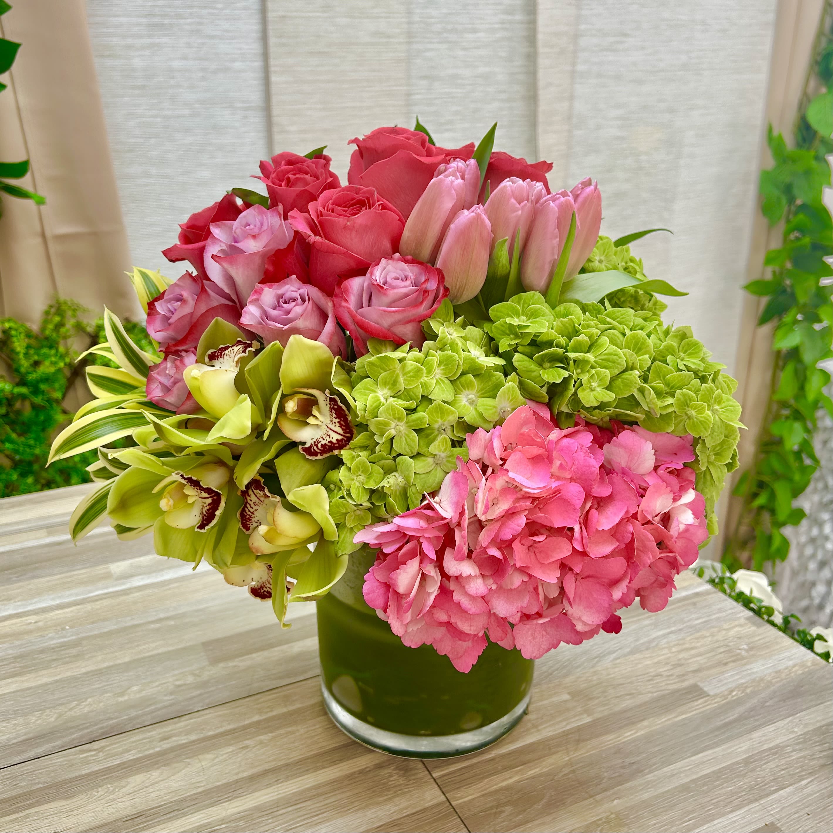 WaterMelon Bouquet - This full, rounded design is tightly clustered for a lush, layered look that reads polished yet garden-fresh. The mix includes hot pink and blush roses, pale pink tulips, green and pink hydrangeas, and green cymbidium orchids arranged in a clear glass vase. The combination of rounded blooms and upright tulips gives the bouquet depth and movement, and the pink-green contrast makes it feel lively and affectionate. 