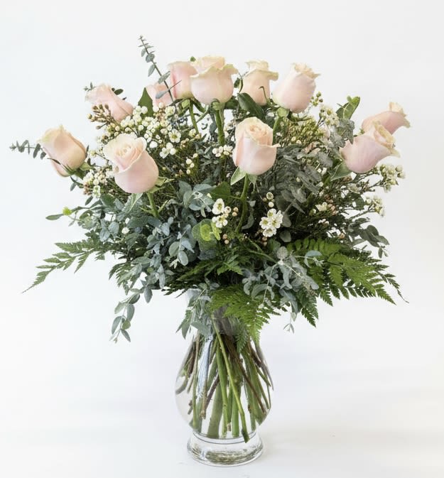 Blush pink roses in a clear glass vase with mixed greenery