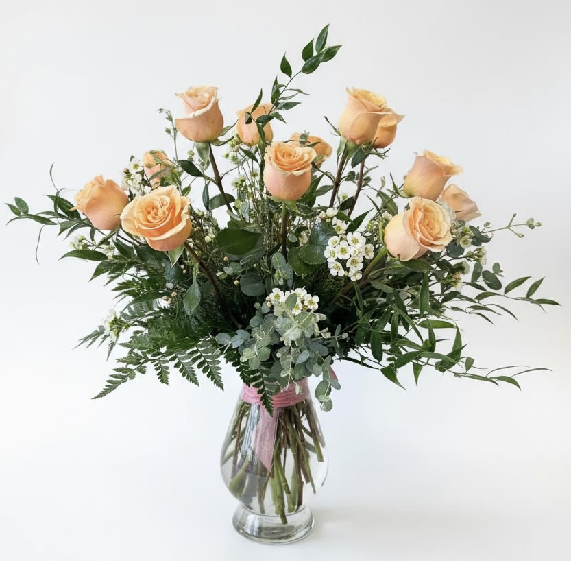 Peach roses in a clear glass vase with mixed greenery