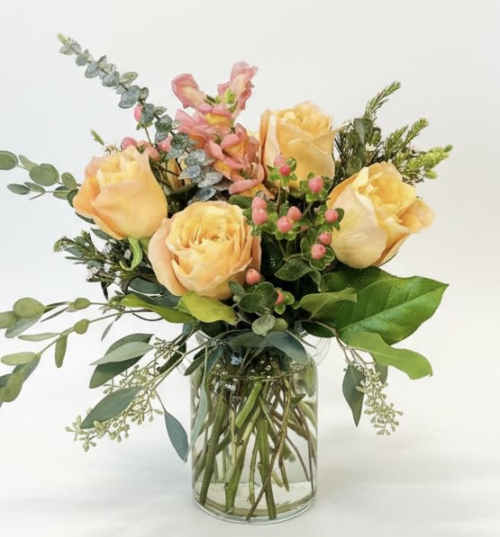 Peach roses arranged in a clear glass vase with mixed greenery