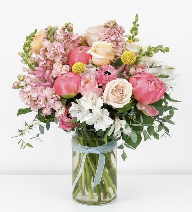 Pink and cream flowers arranged in a glass vase with a blue ribbon.