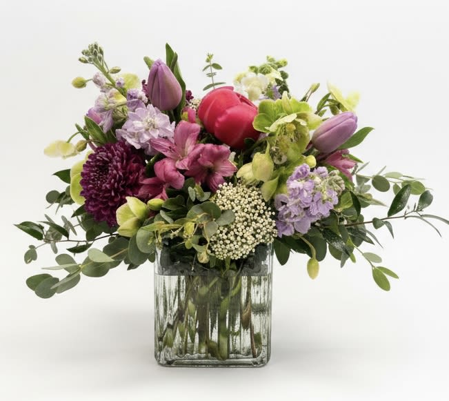 Mixed bouquet of pink, purple, and green flowers in a square glass vase