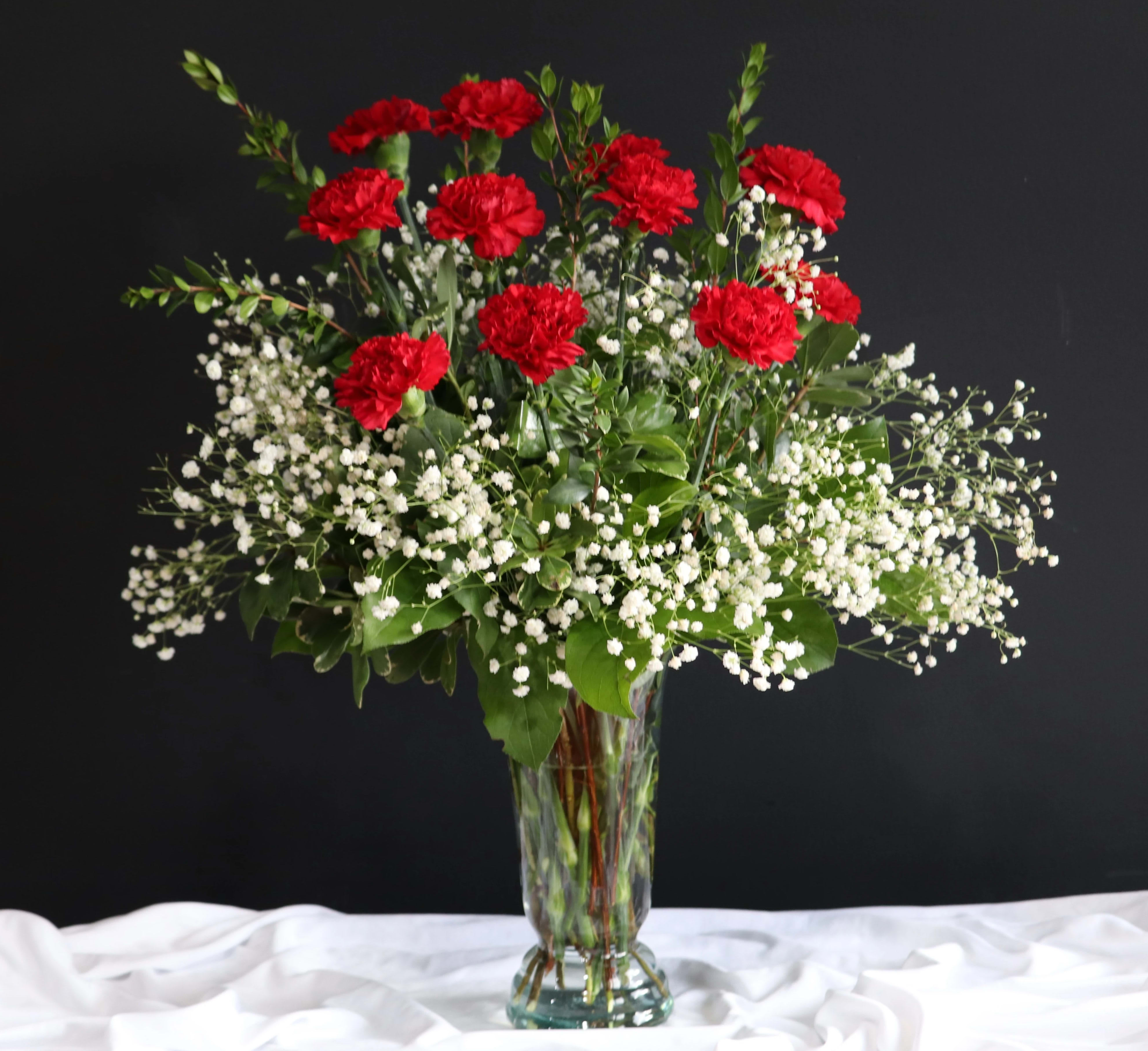 Red carnations and white baby's breath in a clear glass vase