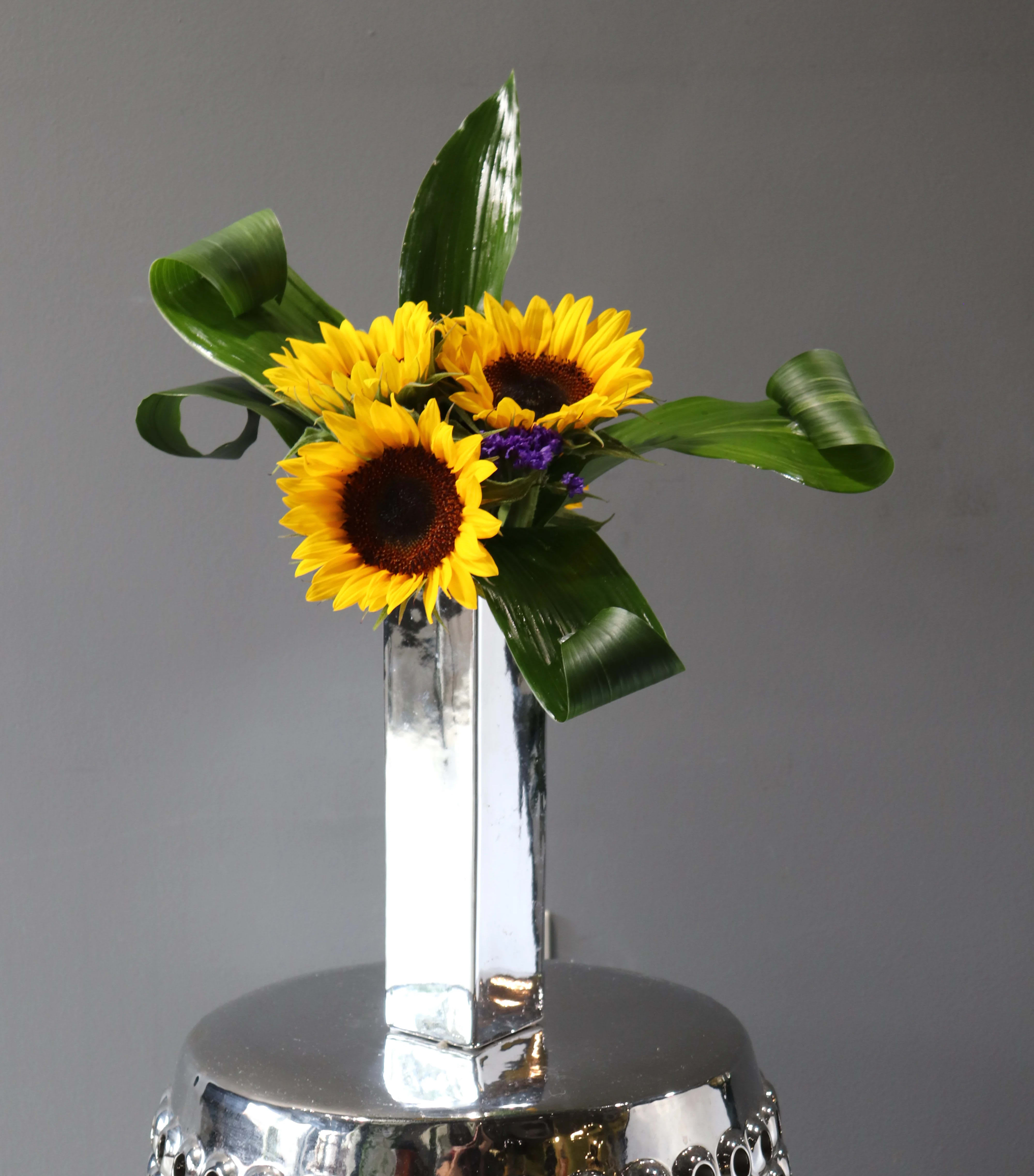 Sunflowers arranged in a tall mirrored vase with curled green leaves