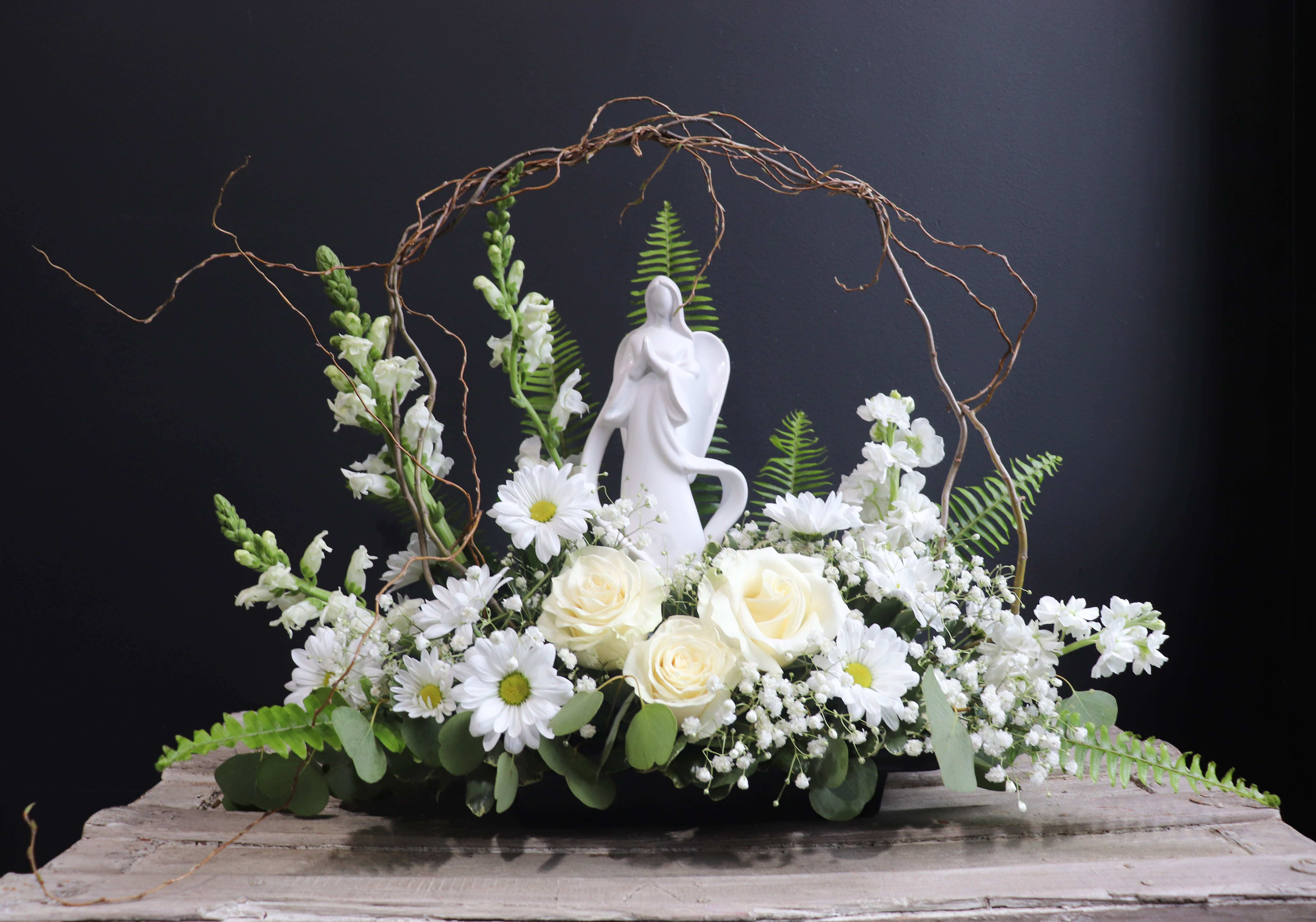 White floral arrangement with roses and daisies around a figurine