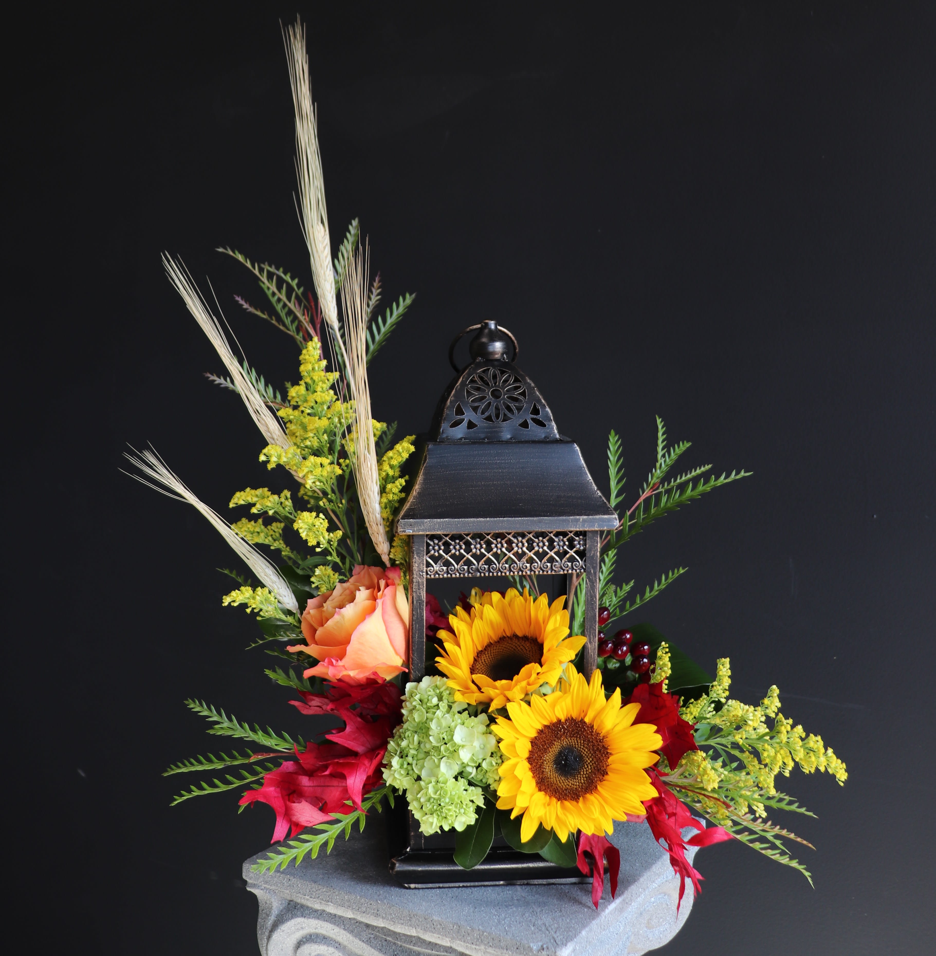 Lantern centerpiece with sunflowers, roses, and mixed foliage