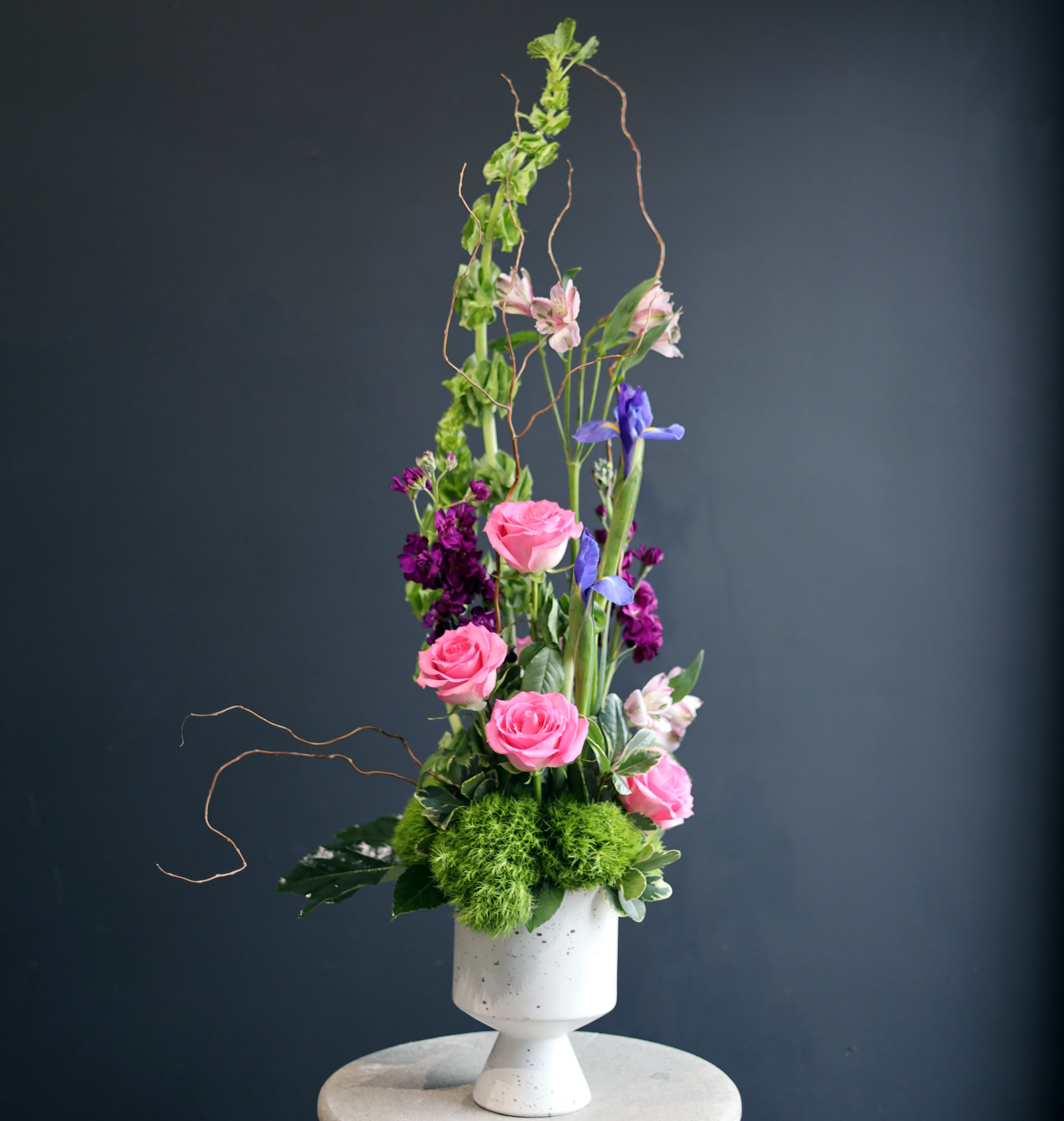 Your Majesty - Here we have an arrangement that stands tall in it's elegance and does not shy away from its viewing! Some of the stems in this arrangement are, but not limited to, Irises, Roses, Alstroemeria, Bells of Ireland, and Curly Willow!