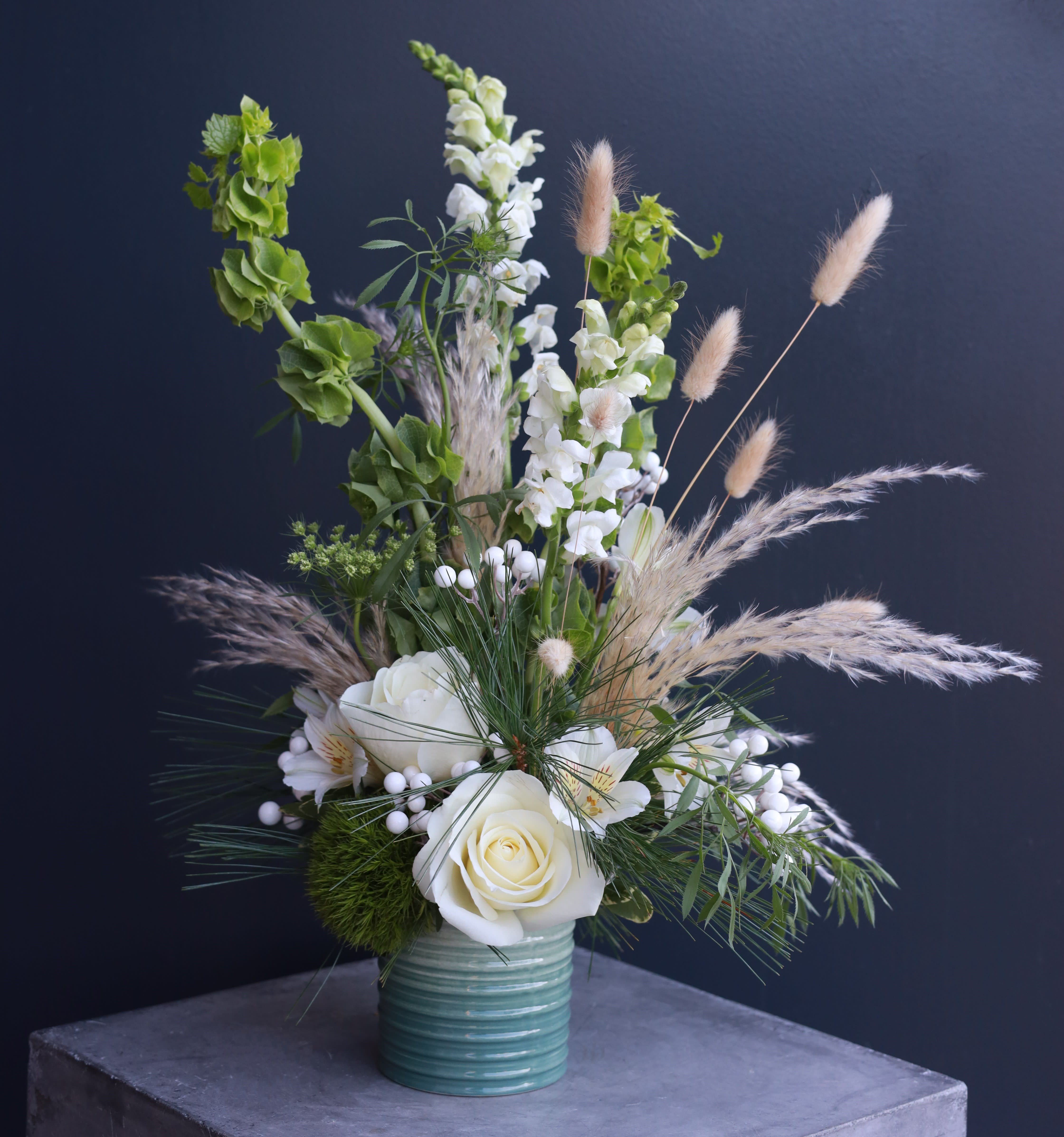 White roses and snapdragons in a teal vase with airy grasses