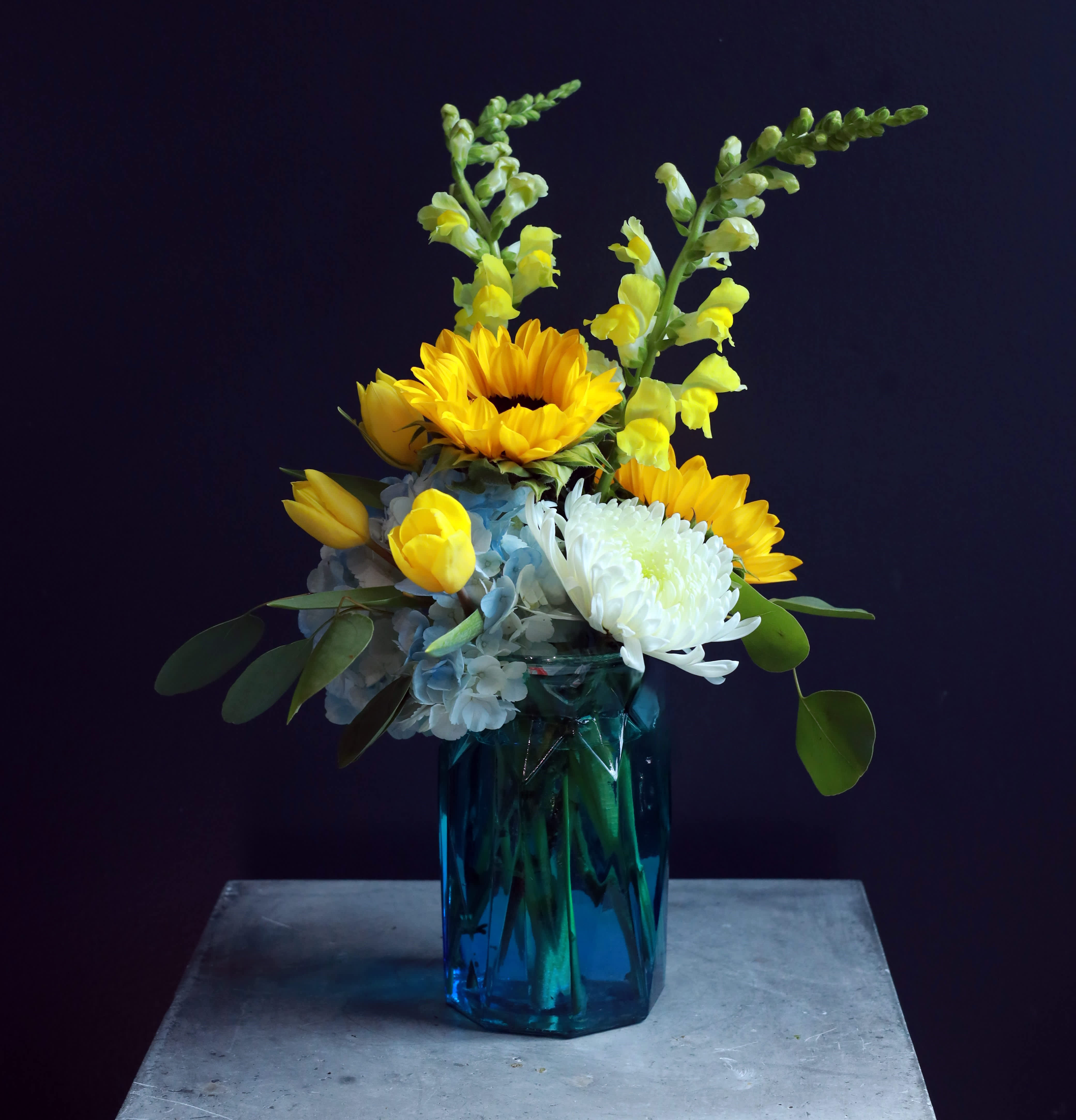 Yellow sunflowers and white blooms in a blue glass vase