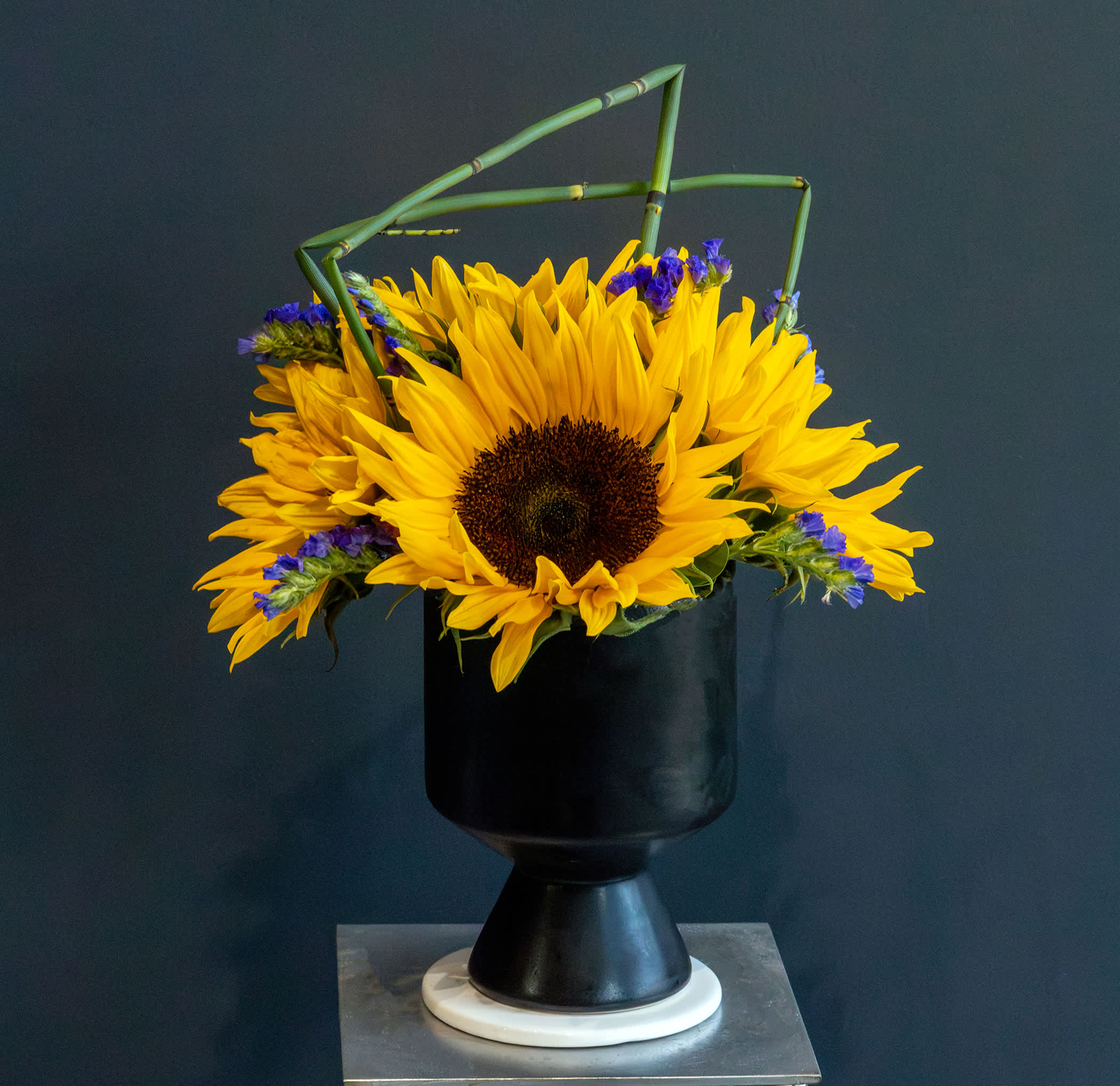 Surreal - A short arrangement filled with fresh cut sunflowers that has a fun twist of bamboo touches that adds surrealism flavor to this artful design.