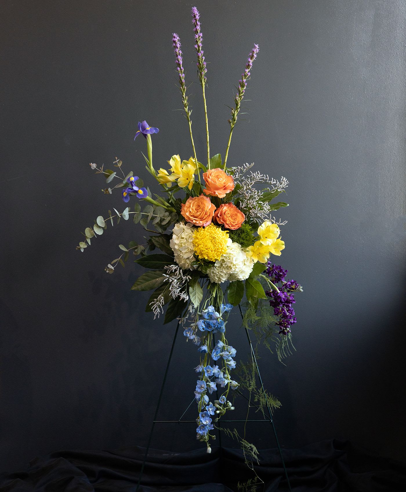 Tall mixed flower arrangement with orange, yellow, blue, and purple blooms