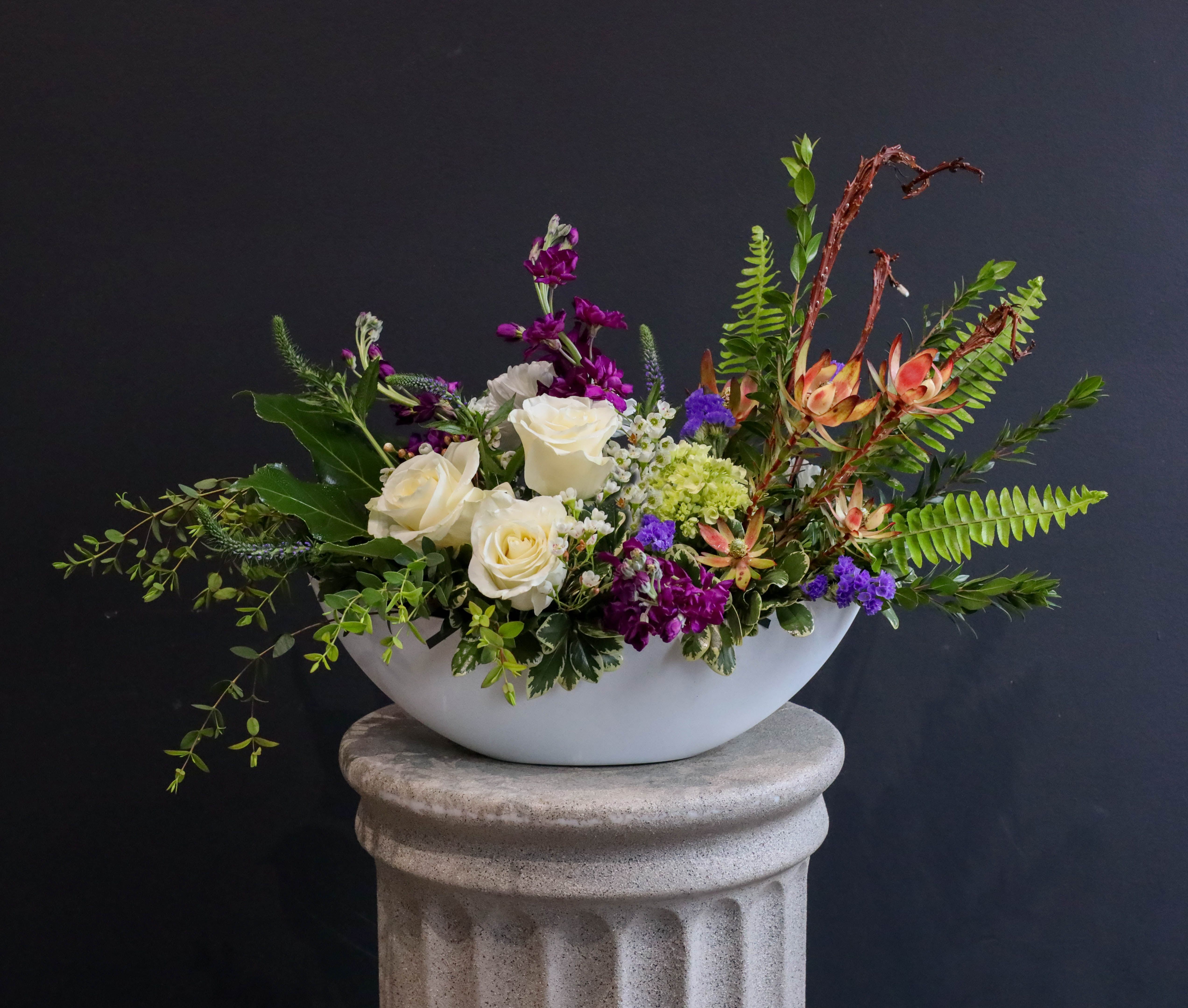 White roses and purple flowers in a white bowl vase