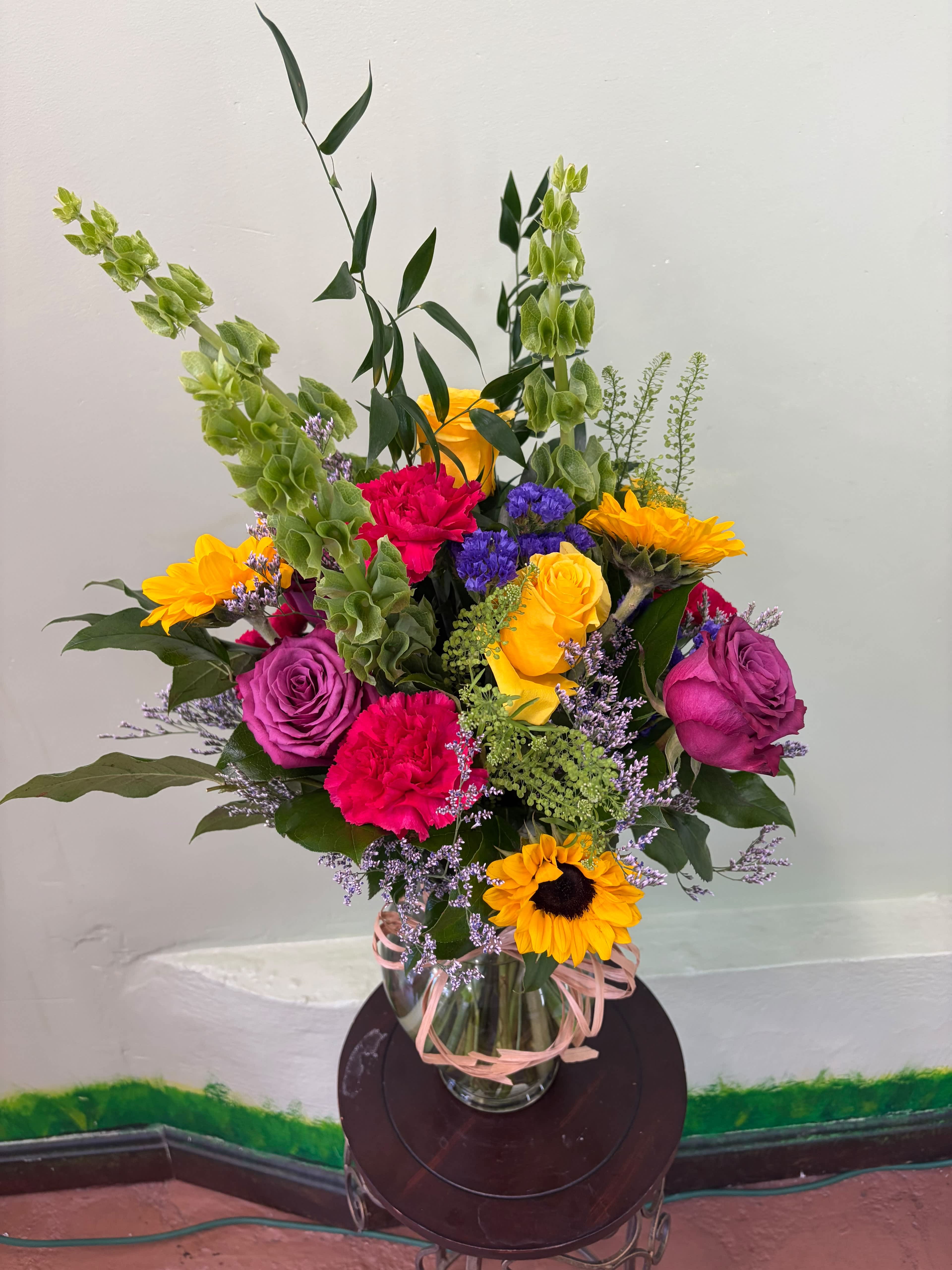 Mixed bouquet of roses, carnations, and sunflowers in a glass vase