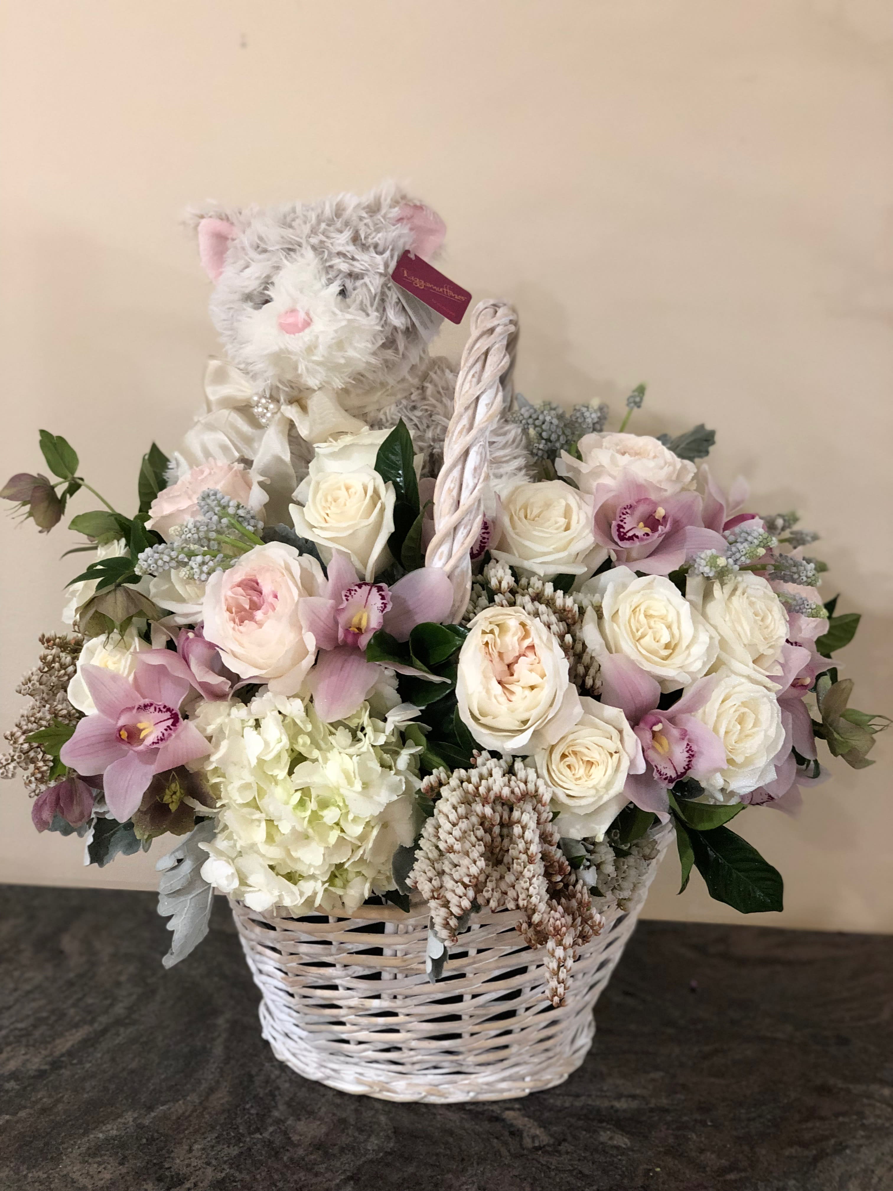 White wicker basket with pastel roses, orchids, and a plush cat