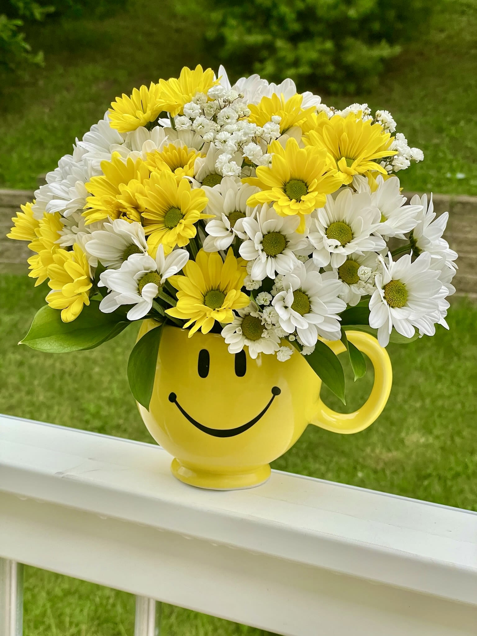 Yellow and white daisy bouquet in a smiley-face mug