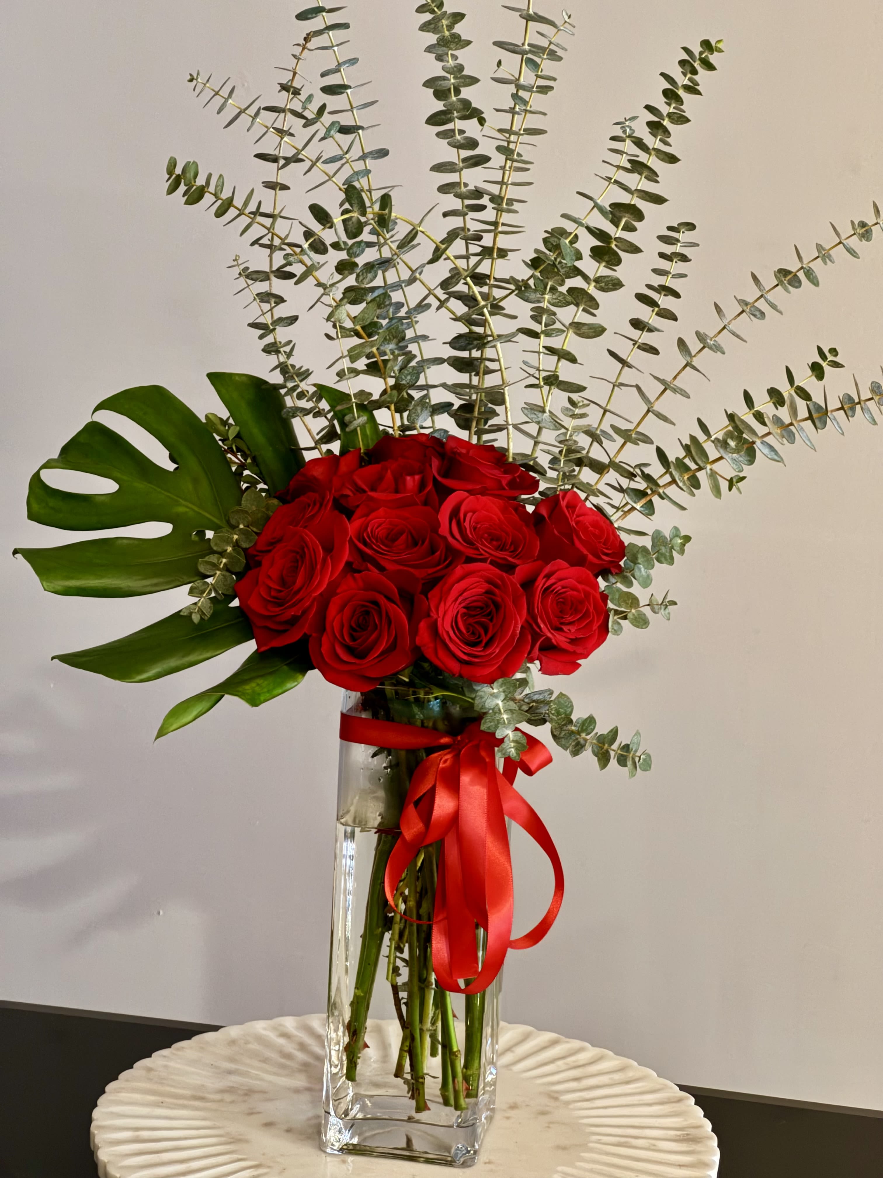 Red roses in a tall glass vase with eucalyptus and a red ribbon