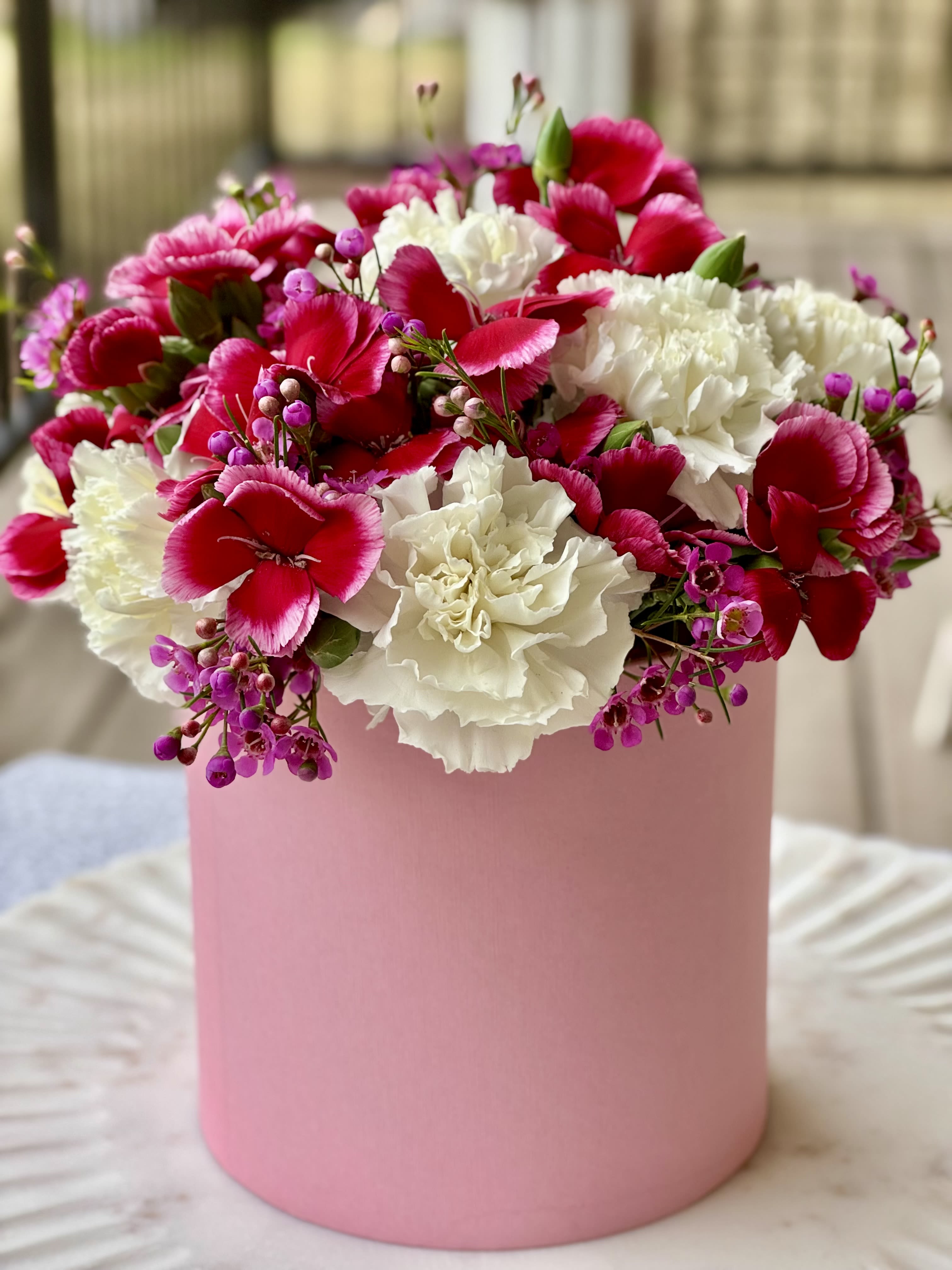 Pink and white carnations with small purple flowers in a pink box