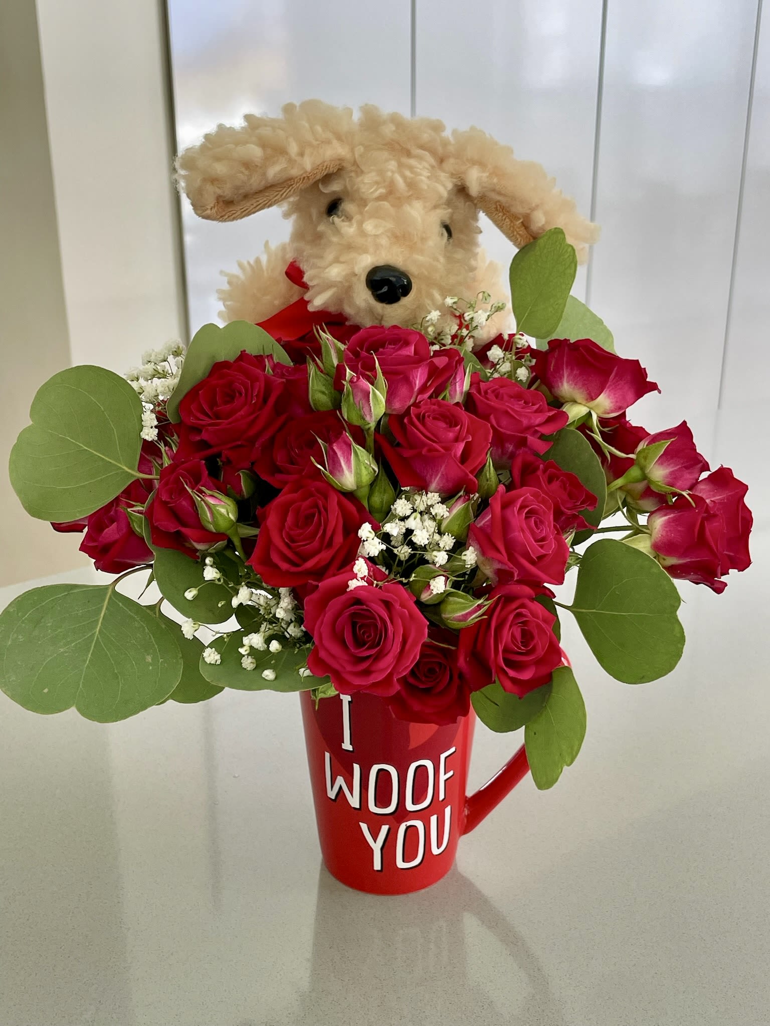 Red roses in a mug with a plush dog peeking over the top