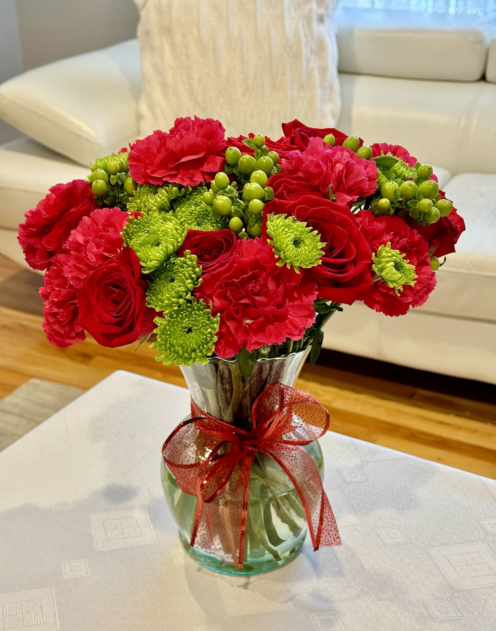 Red roses and pink carnations in a glass vase with a red ribbon