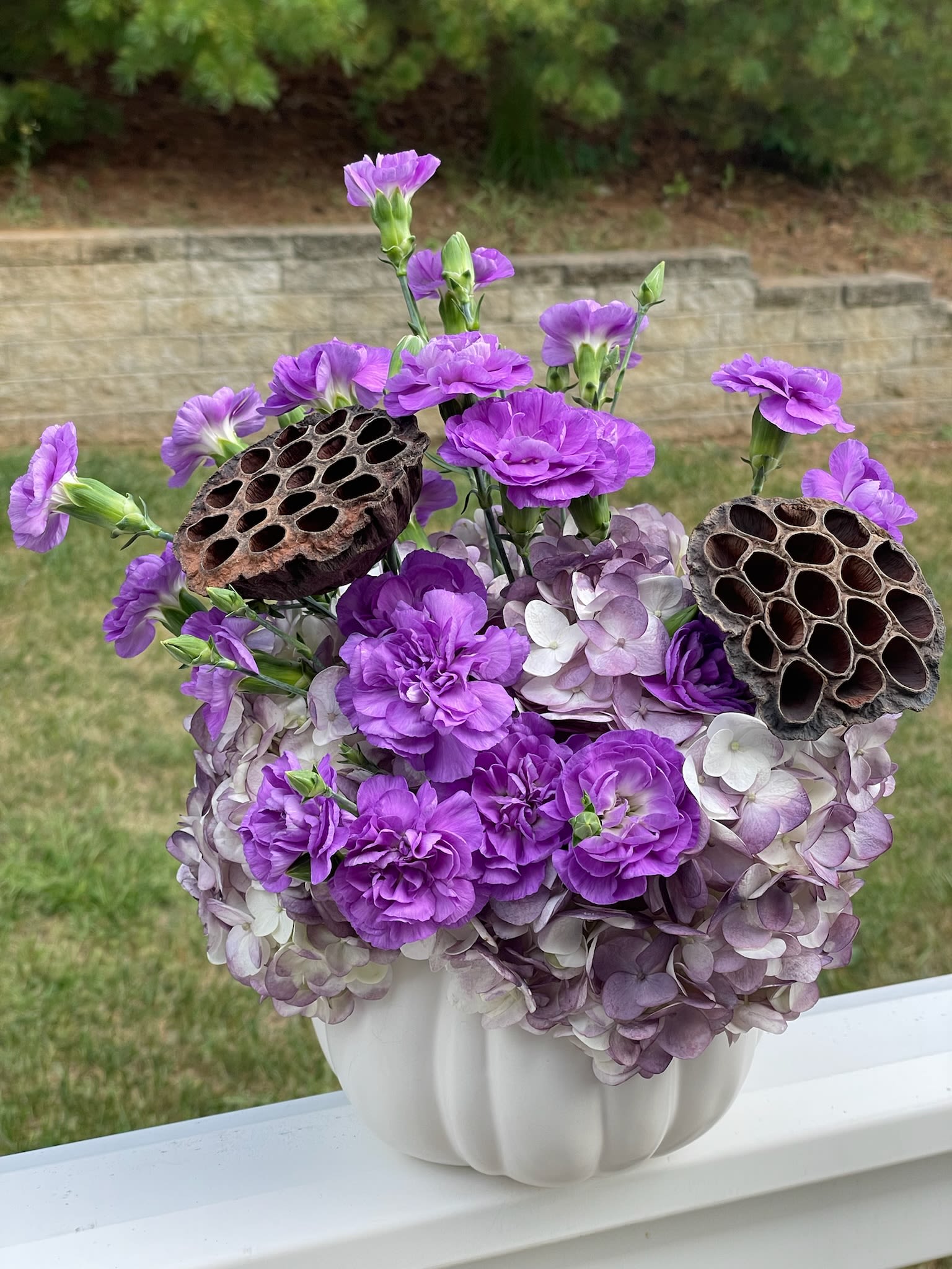 Purple flowers arranged in a white vase with dried seed pods