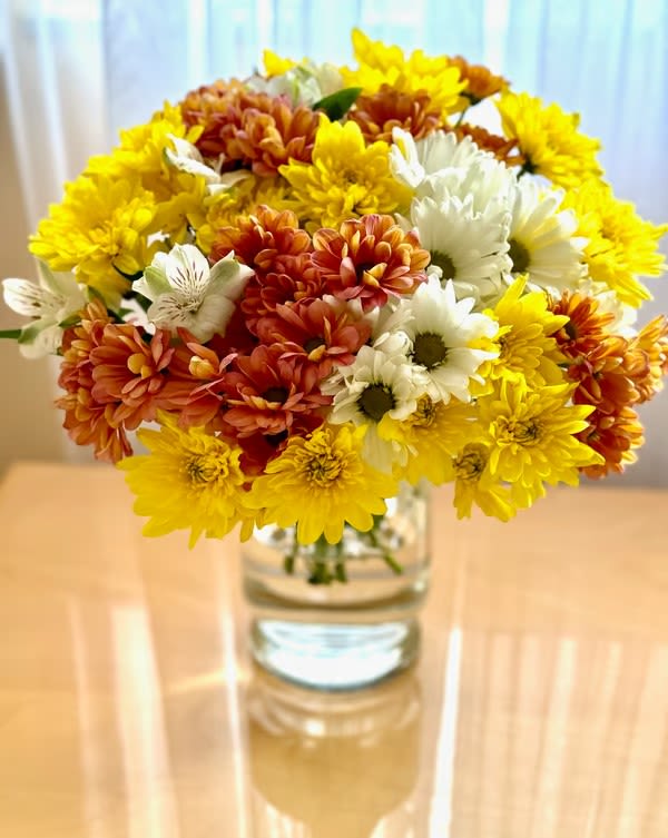 Bouquet of yellow, white, and orange daisies in a clear glass vase
