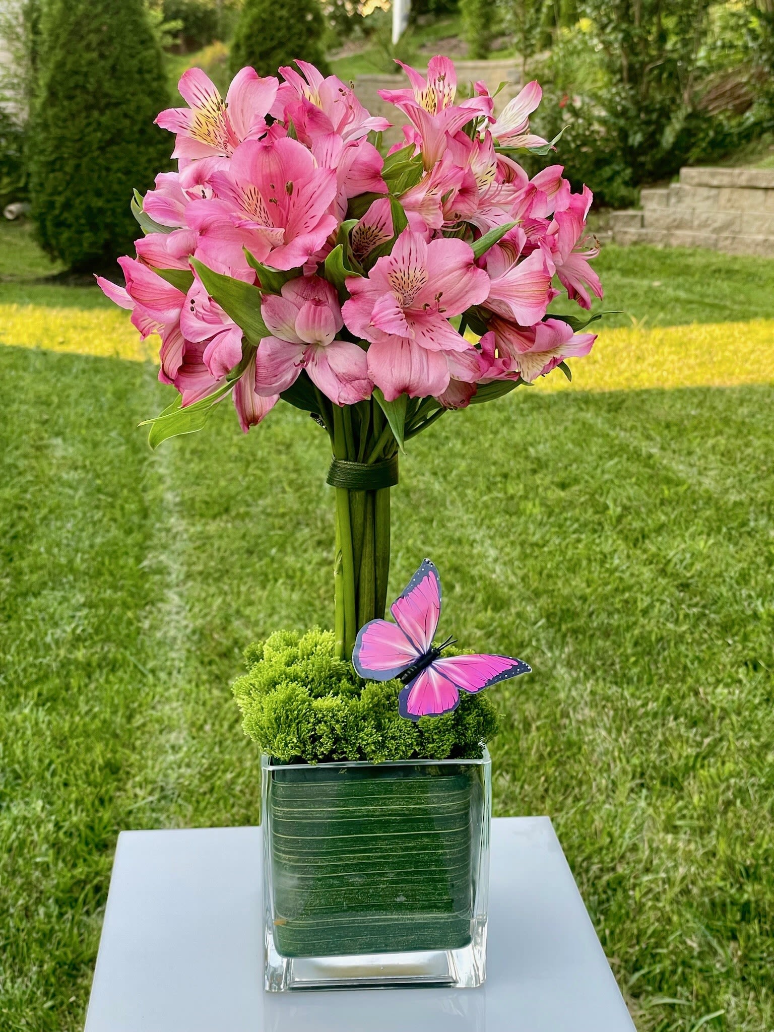 Pink alstroemeria bouquet in a clear square vase with a butterfly accent