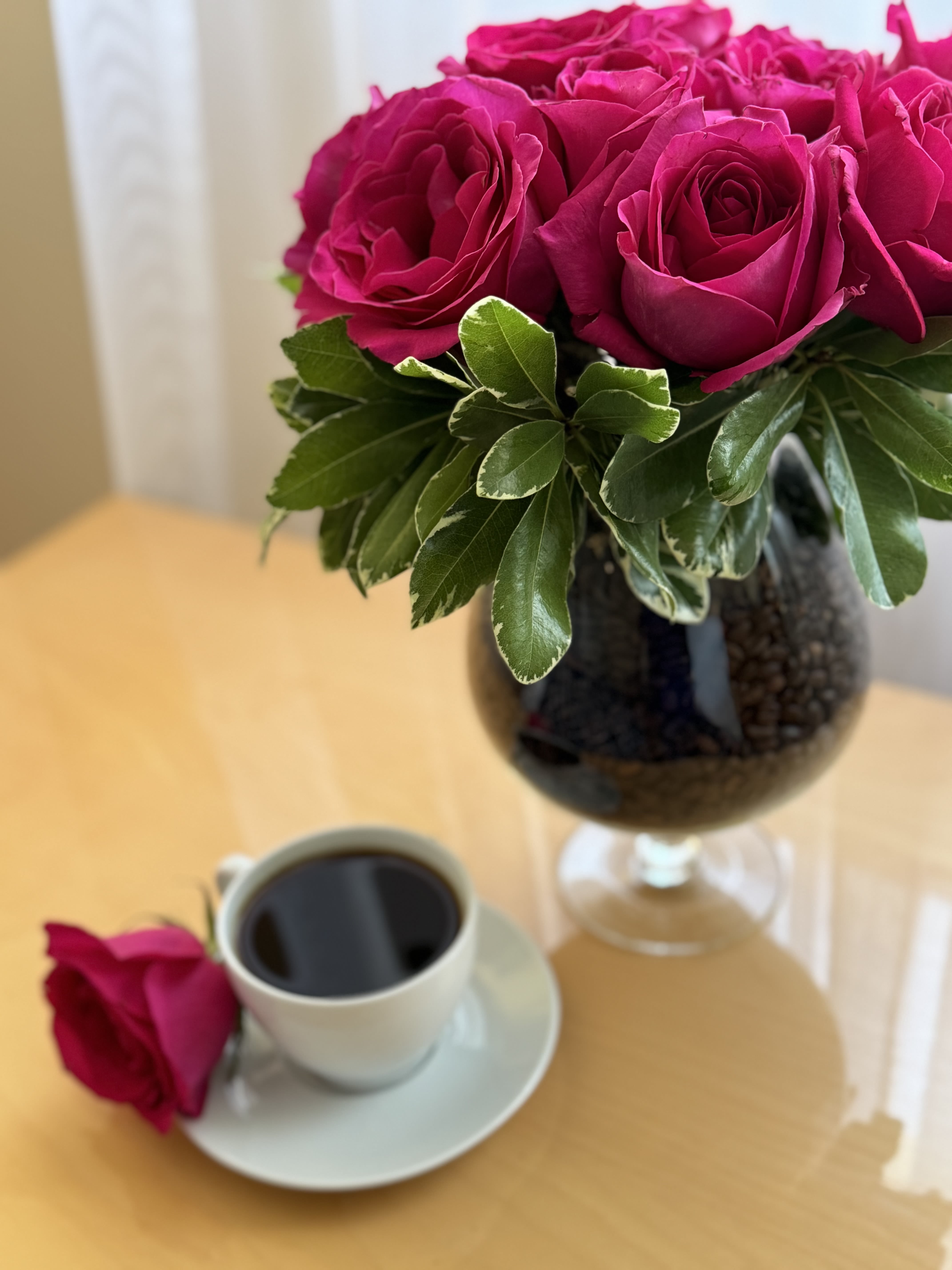Pink roses in a glass vase beside a cup of coffee