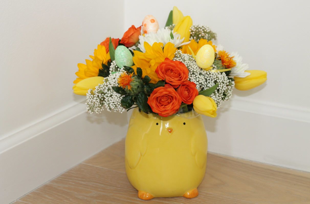 Yellow chick-shaped vase holding a bright mixed flower arrangement