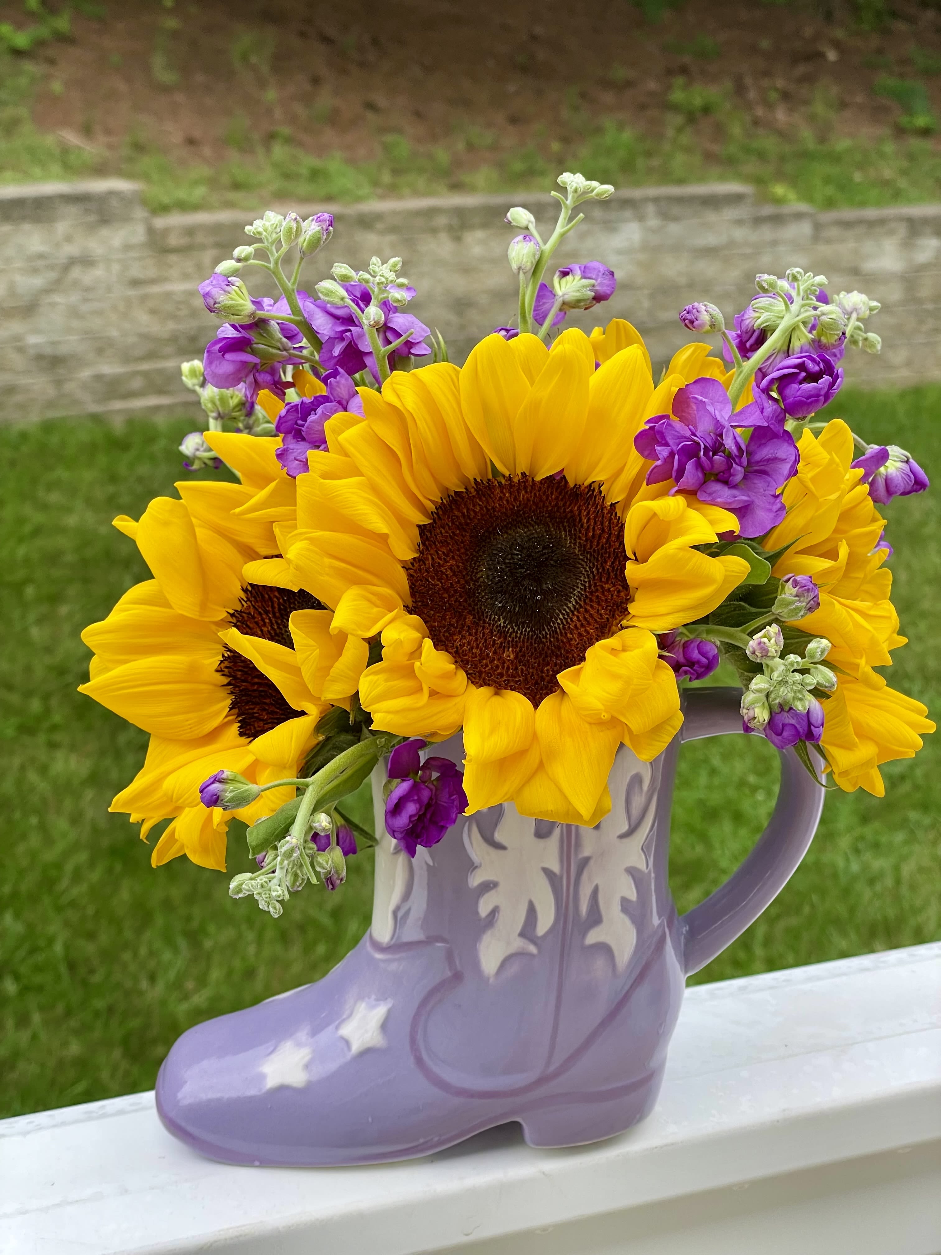 Sunflowers and purple flowers arranged in a lavender boot-shaped vase