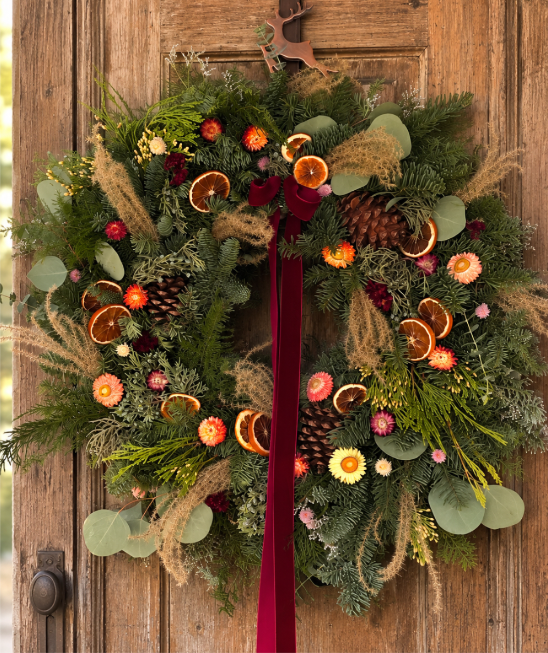 Fresh Holiday Wreath - Pre-order - Designed in our studio on a 20-inch fresh evergreen base, this wreath is thoughtfully layered with premium North Carolina evergreens, dried citrus, natural grasses, pinecones, seasonal flowers, and preserved botanicals. Finished with a luxurious velvet ribbon, each wreath celebrates the quiet beauty of the season with an organic, gathered-from-nature feel.  No two wreaths are exactly alike. Every piece is individually crafted using the freshest available materials while staying true to the overall design and color palette.  Perfect for welcoming guests throughout the holiday season or gifting someone who appreciates timeless, nature-inspired décor.  Available by pre-order only. Limited quantities available.  Dimensions 20" fresh evergreen wreath base Approximately 22" finished diameter depending on natural materials Finished with premium velvet ribbon  Care  Display in a covered outdoor location or indoors away from direct heat sources. Lightly mist the evergreens every few days to help maintain freshness. As the season progresses, the fresh foliage will naturally dry while retaining its rustic character.
