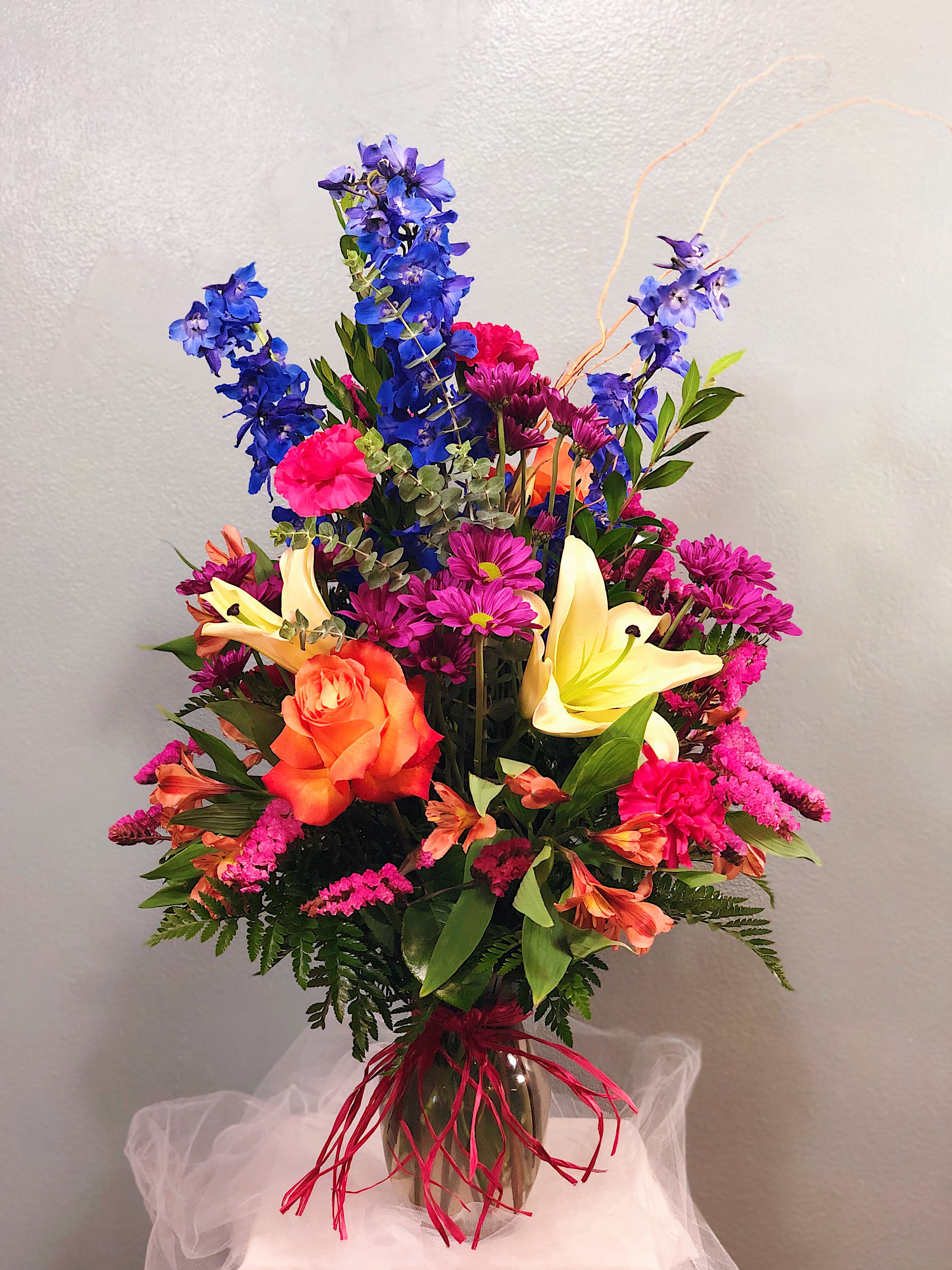 Colorful bouquet with blue delphinium, orange roses, and yellow lilies in a vase