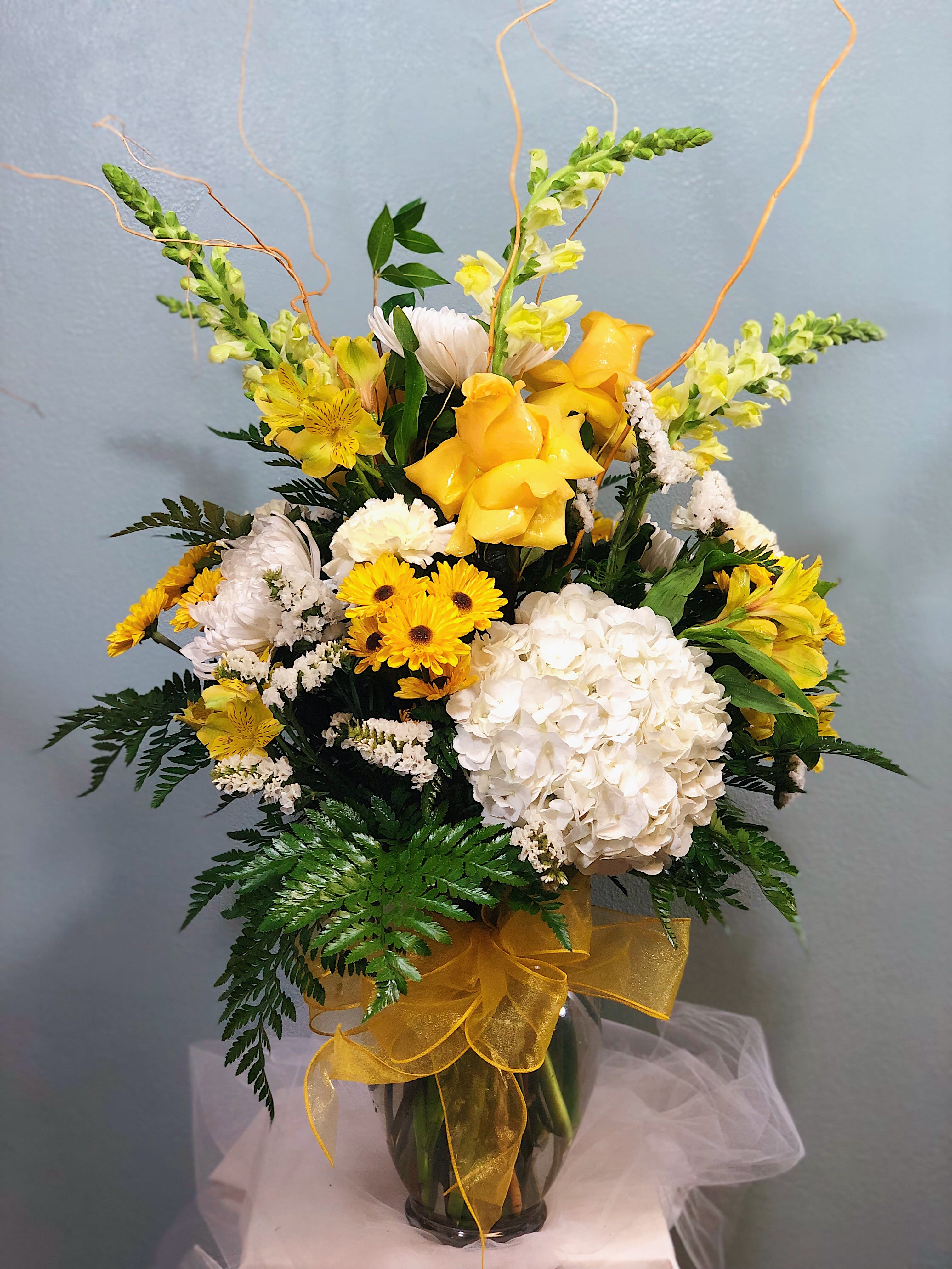 Yellow and white floral arrangement in a glass vase with ribbon