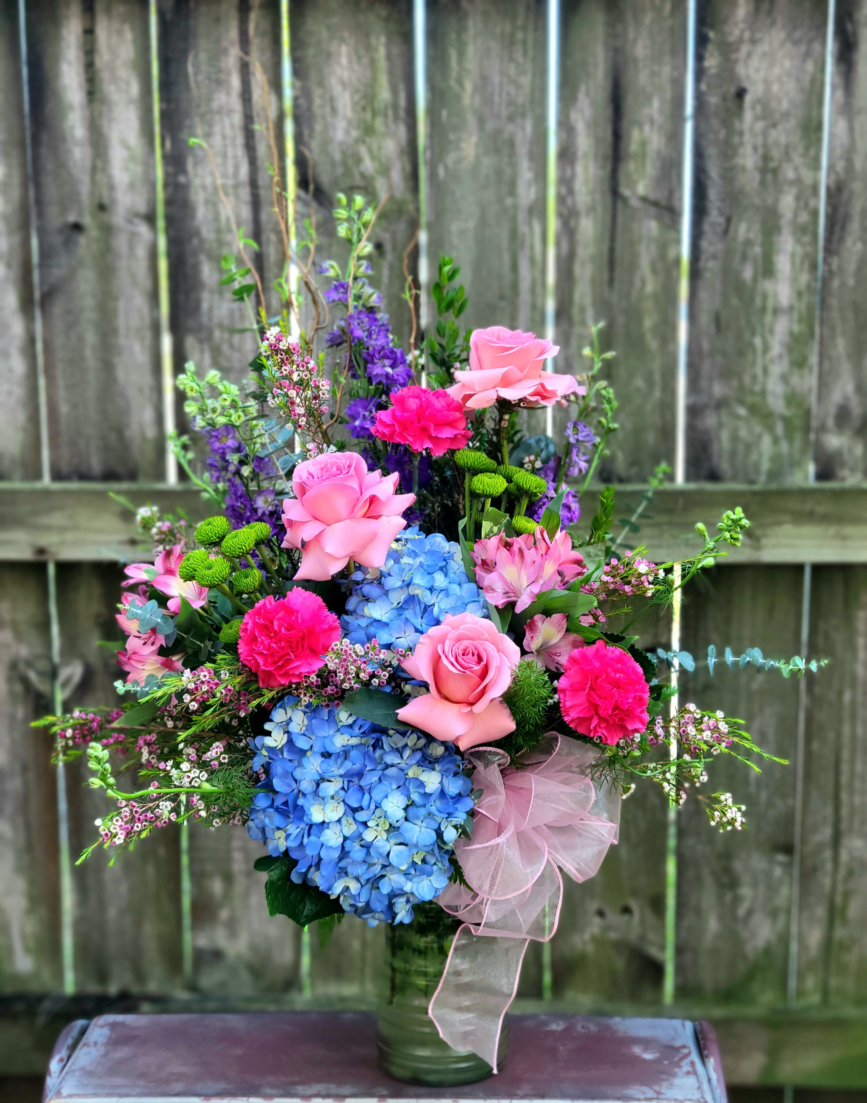Pink and blue floral arrangement in a glass vase with a ribbon bow