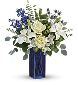 White lilies and roses in a tall blue vase with blue flowers