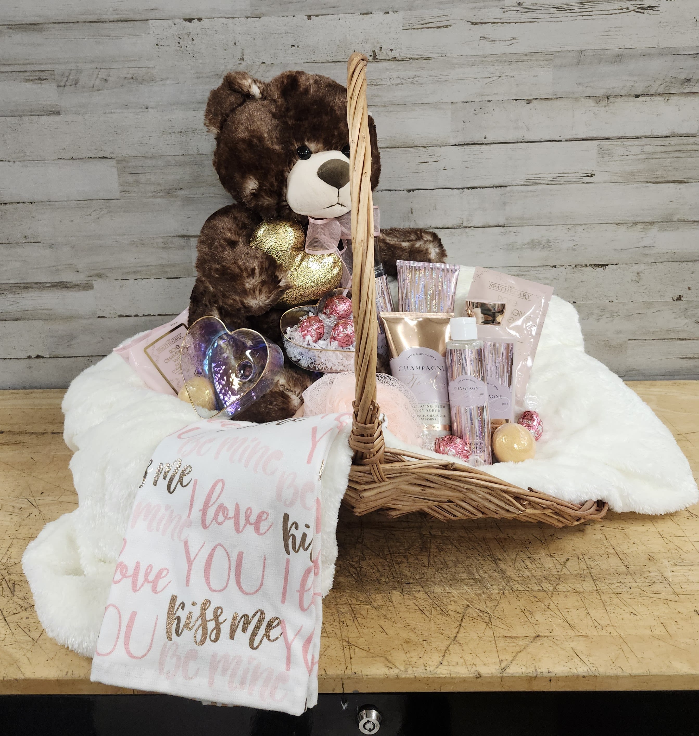 Gift basket with a teddy bear, chocolates, and beauty items on a white blanket