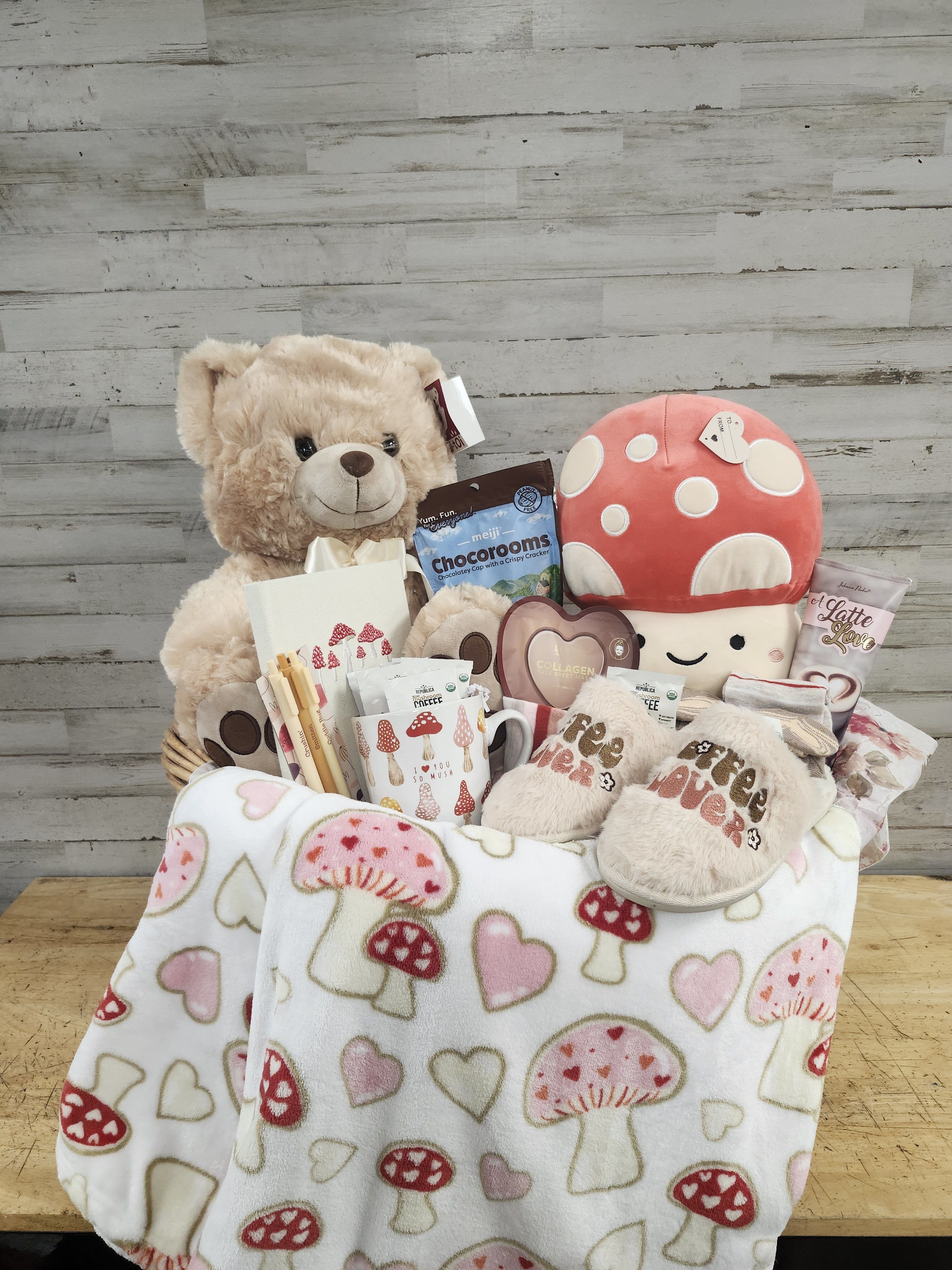 Gift basket with a teddy bear, mushroom plush, snacks, and a heart-patterned blanket