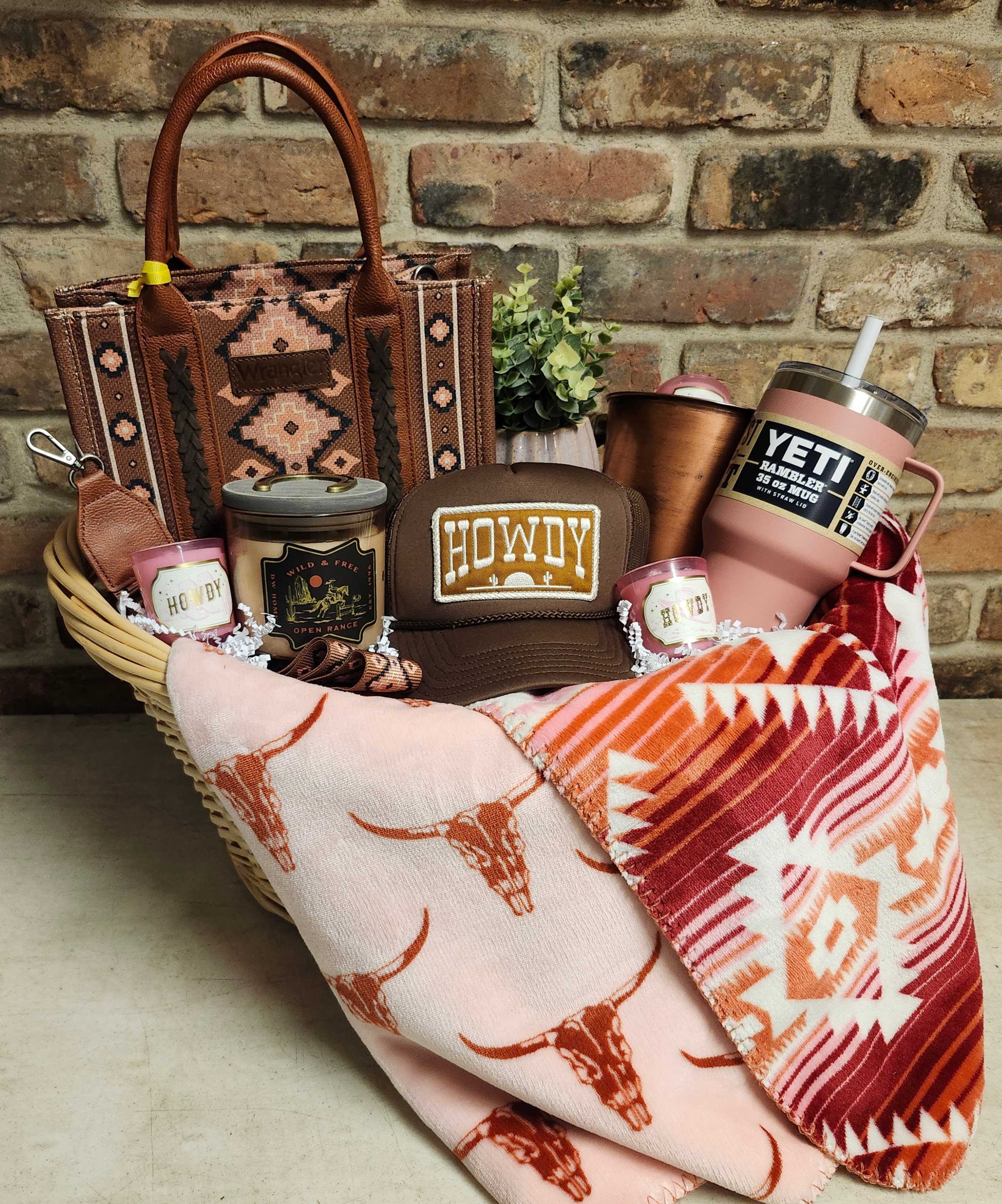 Gift basket with a patterned tote, tumblers, candles, a cap, and folded blankets