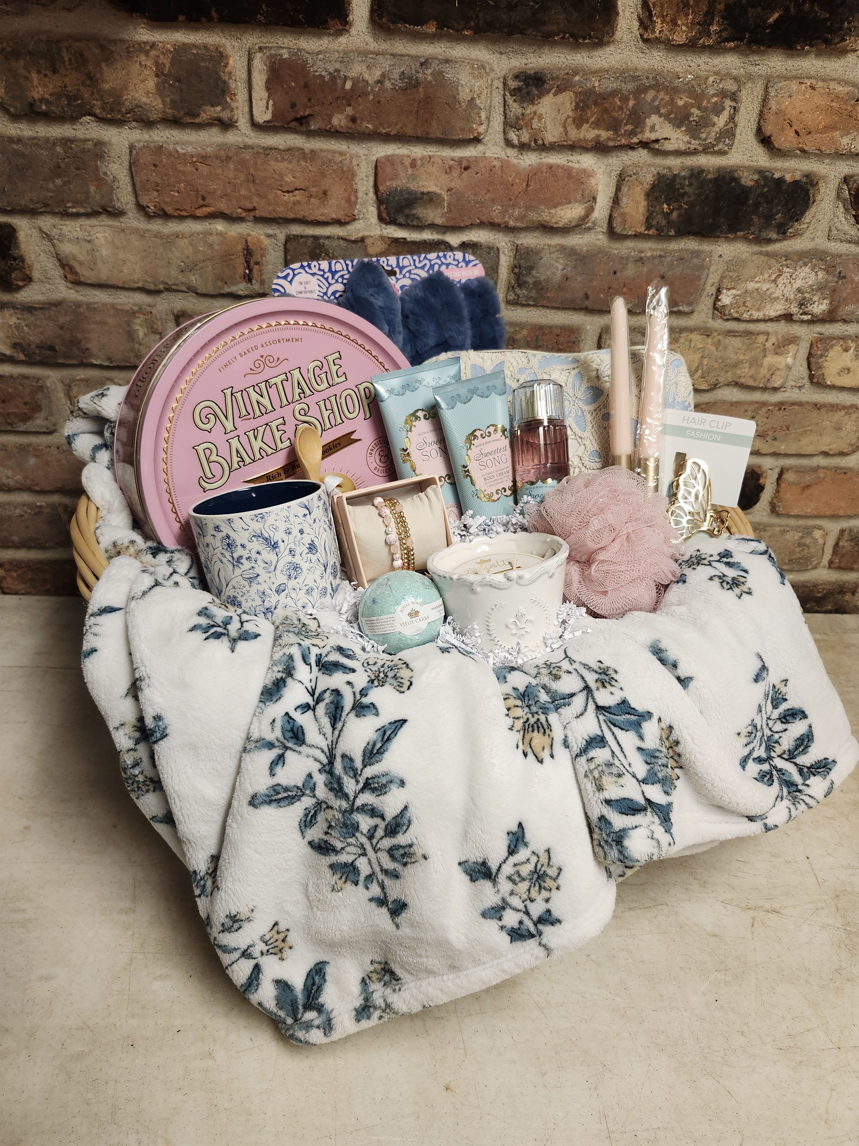Gift basket with candles, bath items, and accessories on a floral blanket