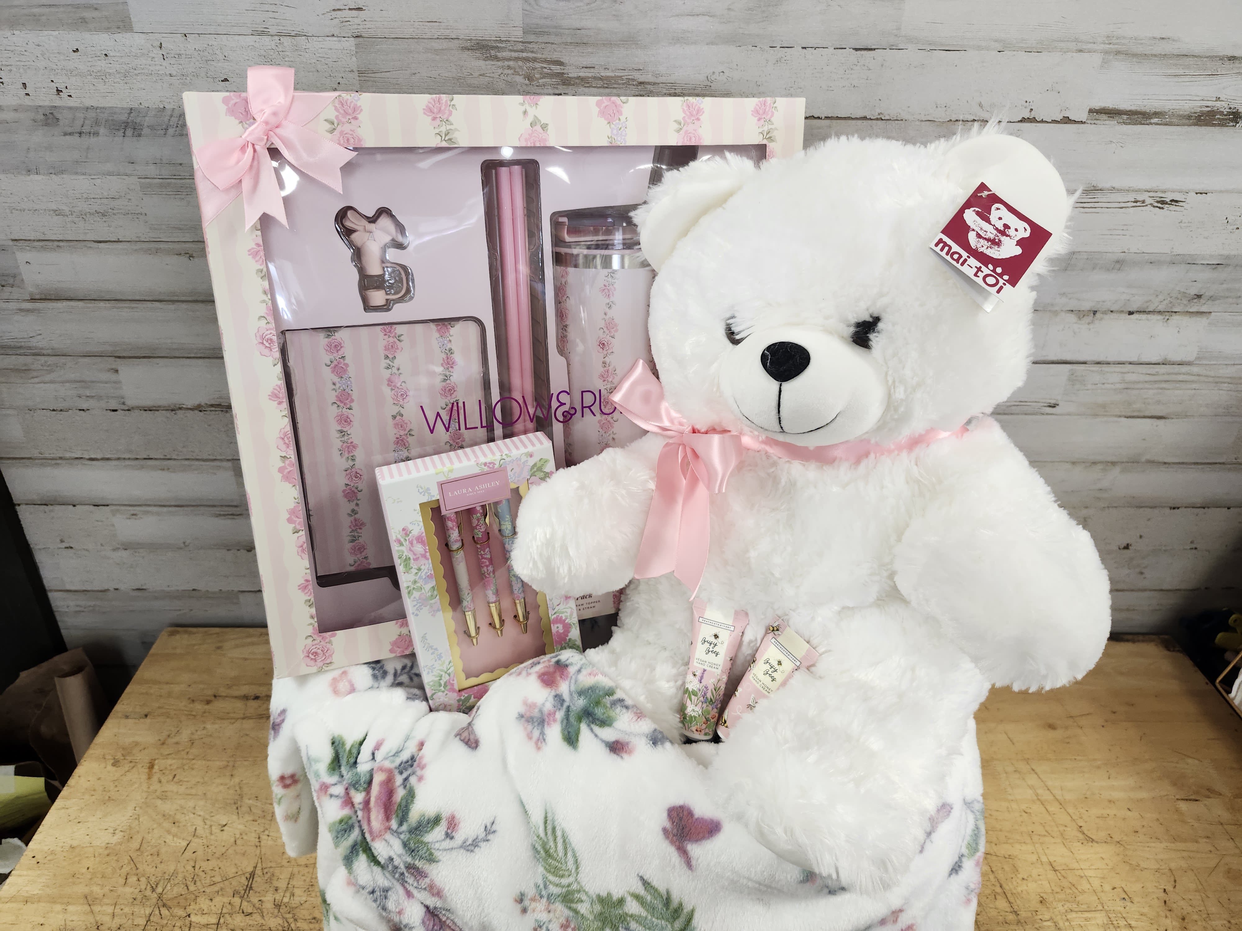White teddy bear with a pink ribbon beside a floral gift set