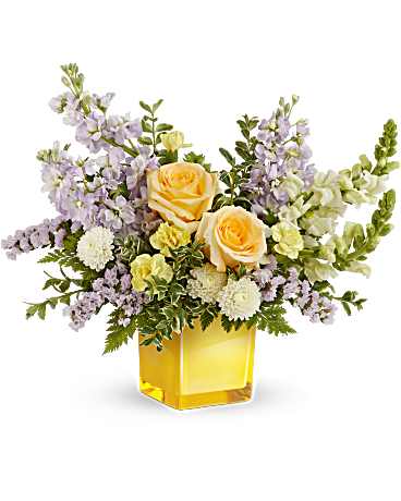 Yellow roses and lavender flowers in a square glass vase