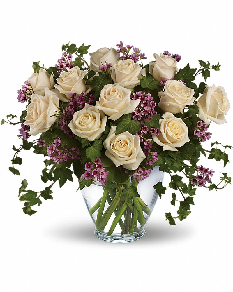 Cream roses and purple filler flowers in a clear glass vase