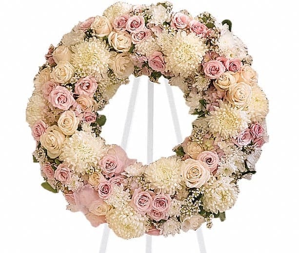 Round floral wreath of pale pink and cream roses on a white stand