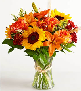 Bouquet of sunflowers, orange lilies, and roses in a clear glass vase