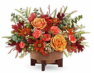 Autumn floral arrangement with orange roses and red blooms in a low container