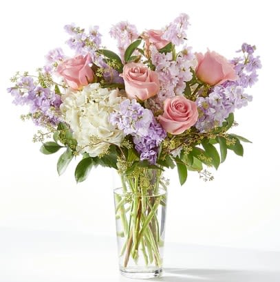 Tall glass vase of pink roses, white hydrangea, and lavender blooms in a loose pastel arrangement