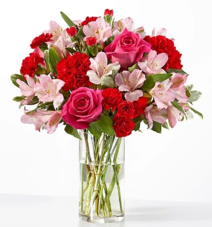 Pink roses, red carnations, and light pink alstroemeria in a clear glass vase