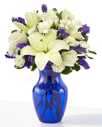 White lilies and roses in a blue glass vase with purple accents