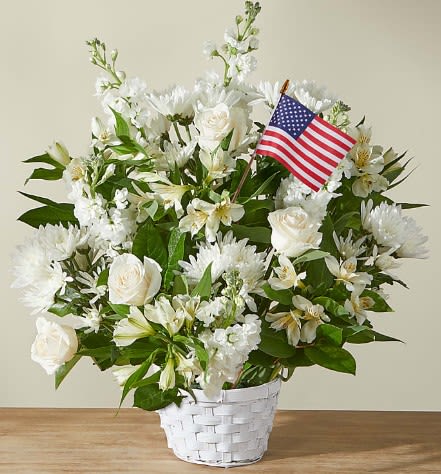 White floral arrangement in a white basket with a small American flag